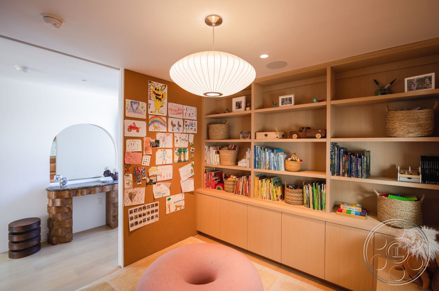 Modern 519 - interior wooden bookshelf with open shelving, interior cork wall art display, interior round paper pendant light, interior stone accent column, interior playful round pink carpet, interior built-in cabinetry with soft close doors, interior light wood flooring, interior decorative woven storage baskets, interior arched entryway, interior children’s playroom