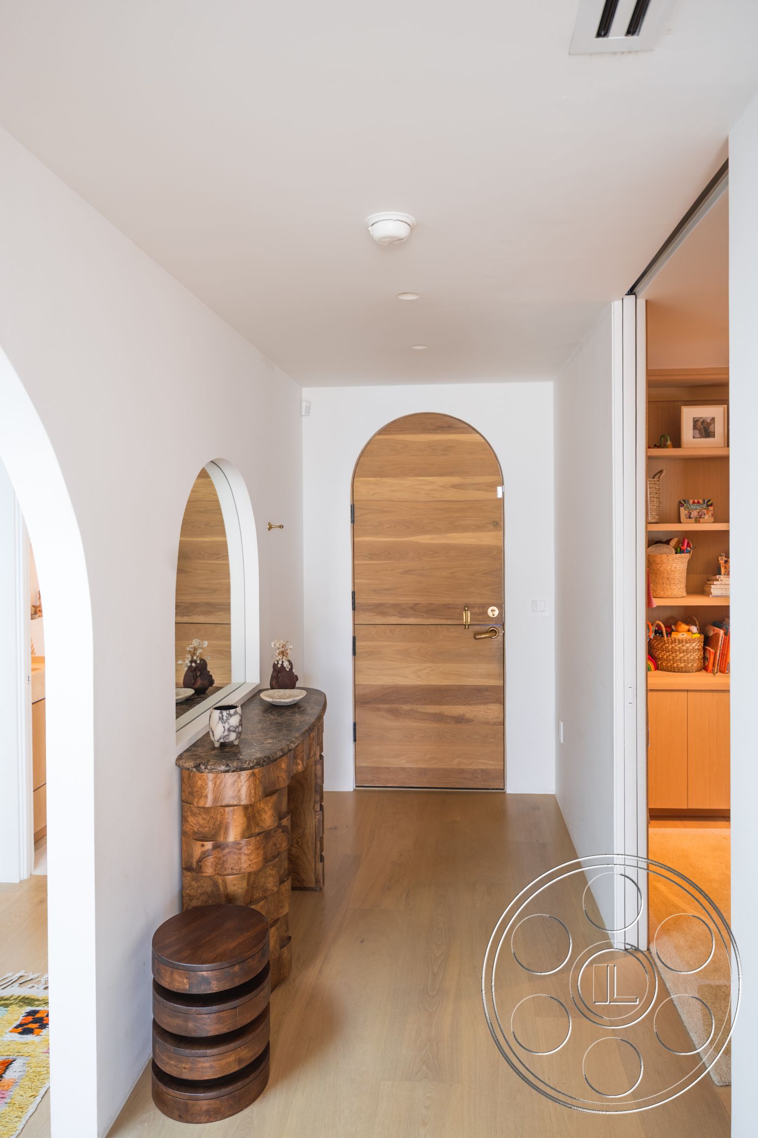 Modern 519 - soft neutral color palette, light hardwood flooring, recessed ceiling lighting, modern interior design, natural wood console table, smooth plaster walls, minimalist entryway design, contemporary home entrance, interior wood door, interior curved archways, solid wood round stools, decorative mirror accent, organic shapes in furniture