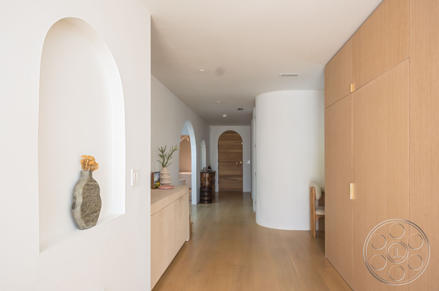Modern 519 - neutral color palette, soft natural light, integrated storage solutions, clean lines and geometric forms, exterior white stucco walls, contemporary interior architecture, smooth plaster wall finishes, open hallway layout, modern minimalist design elements, interior wood paneling cabinets, arched doorways with rounded tops, natural wood hallway flooring, arched niche with decorative vase, curved wall structure, bronze door hardware, compact entryway with functional decor