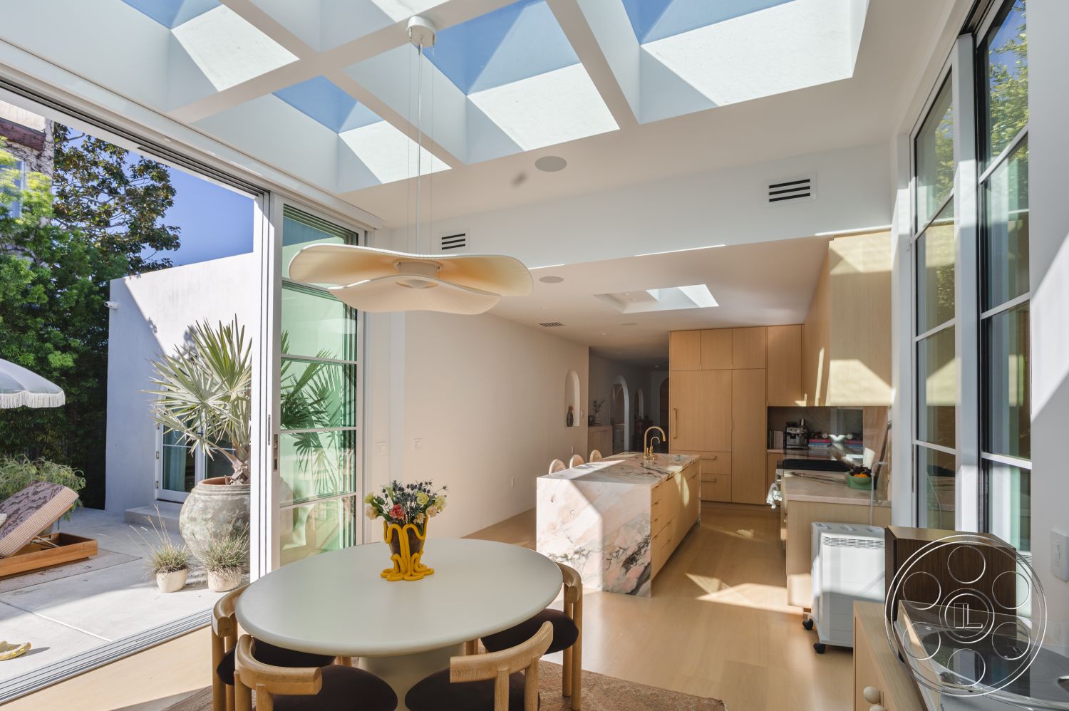 Modern 519 - open concept living space, modern pendant light fixture, minimalist design with clean lines, potted plants for interior greenery, interior kitchen with marble island, concrete floor in kitchen area, large glass sliding doors for natural light, wooden cabinets with a light finish, sky light ceiling panels for illumination, rounded dining table with wooden chairs, neutral color palette in decor, exposed wood accents in ceiling, smooth wall treatments with white paint, suburban backyard setting visible through glass, integrated appliances in kitchen design, floating shelves for kitchen storage, folding glass doors to merge indoor and outdoor space