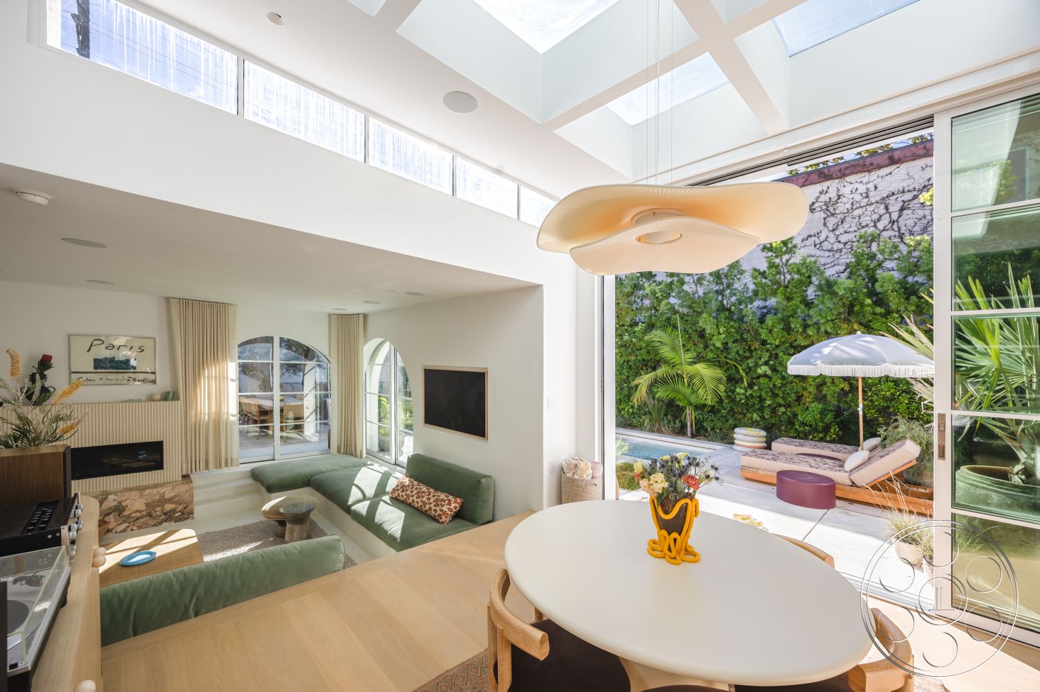 Modern 519 - interior open floor plan, interior neutral color palette, interior hardwood flooring, interior recessed ceiling lights, interior glass sliding doors, exterior outdoor lounge area, interior modern sectional sofa, interior contemporary pendant light, interior textured wall panels, exterior outdoor seating, interior decorative wall art, interior bright natural light, exterior concrete patio surface, interior arched windows, interior built-in wall cabinetry, interior dining area with round table, exterior sunshade umbrella, exterior greenery backdrop, exterior smooth concrete borders, interior ceiling skylights