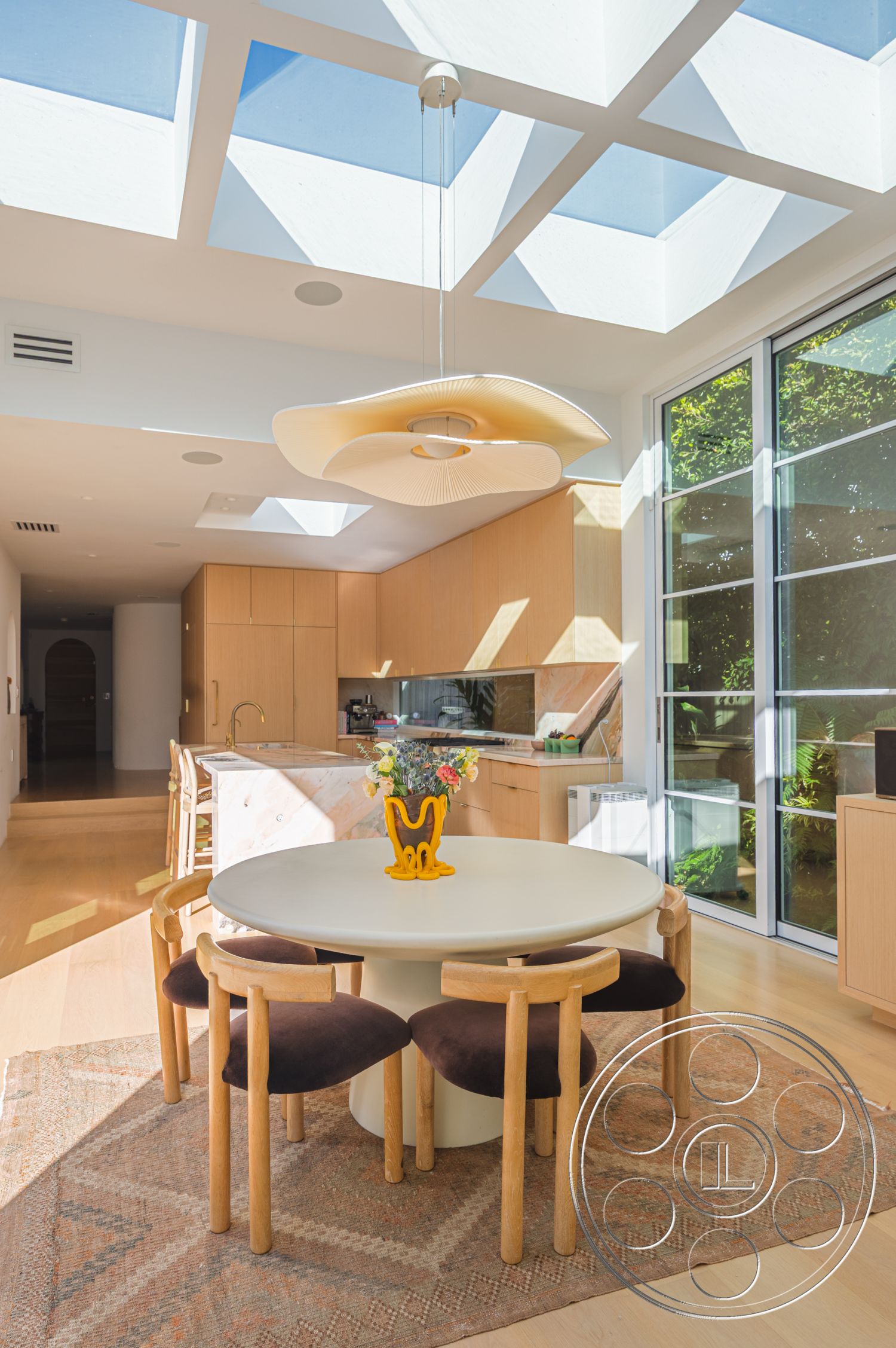 Modern 519 - neutral color palette, indoor plants, textured area rug, open concept layout, large glass windows, light wood cabinetry, round dining table, marble kitchen countertop, minimalist pendant lighting, modern architectural details, hardwood dining room floors, bright and airy interior, mid-century modern dining chairs, geometric skylight ceiling, kitchen island with bar seating