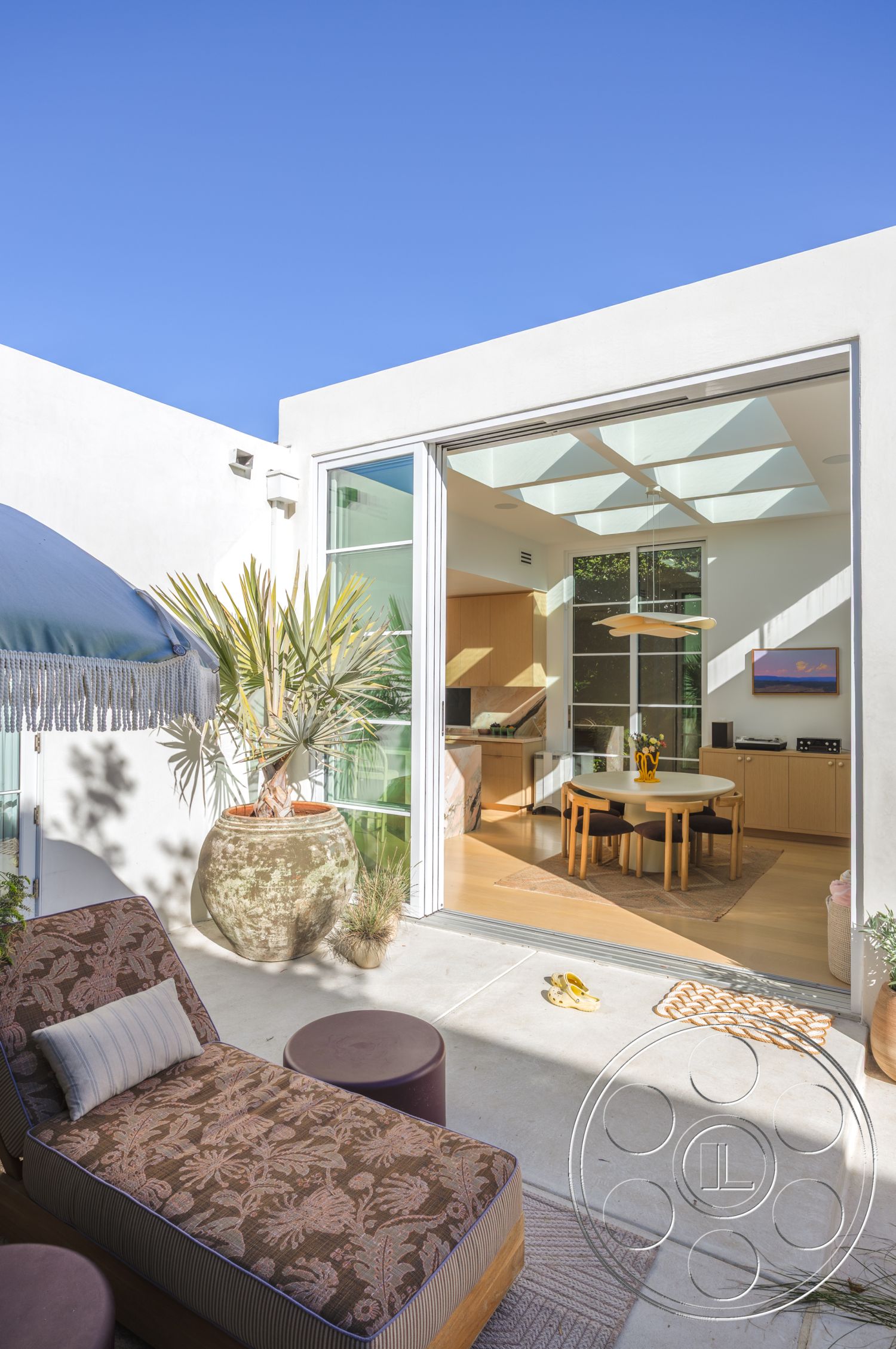 Modern 519 - modern outdoor furniture, light wood cabinetry, smooth concrete surface, open-concept layout, sunlit interior, casual outdoor seating area, suburban backyard setting, minimalist interior design, exterior concrete patio flooring, glass sliding door with panoramic view, wooden dining table with round shape, plant pot with tropical foliage, fabric lounge chair with floral pattern, natural light flooding living space, decorative rug in dining area, decorative woven basket, suspended ceiling light fixture