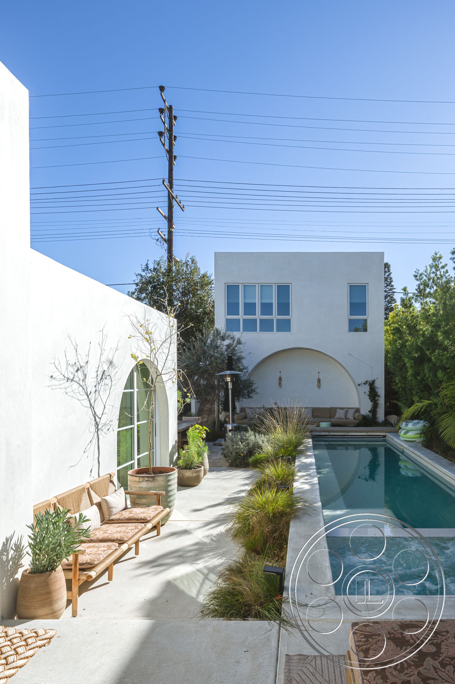 Modern 519 - exterior, white stucco walls, large glass windows, rectangular swimming pool, urban environment, clear blue sky, desert landscaping, lush vegetation, arched doorway, sunny outdoor area, concrete pool deck, outdoor lounge space, concrete patio flooring, minimalist architectural style, wooden outdoor seating, modern garden planters, horizontal power lines