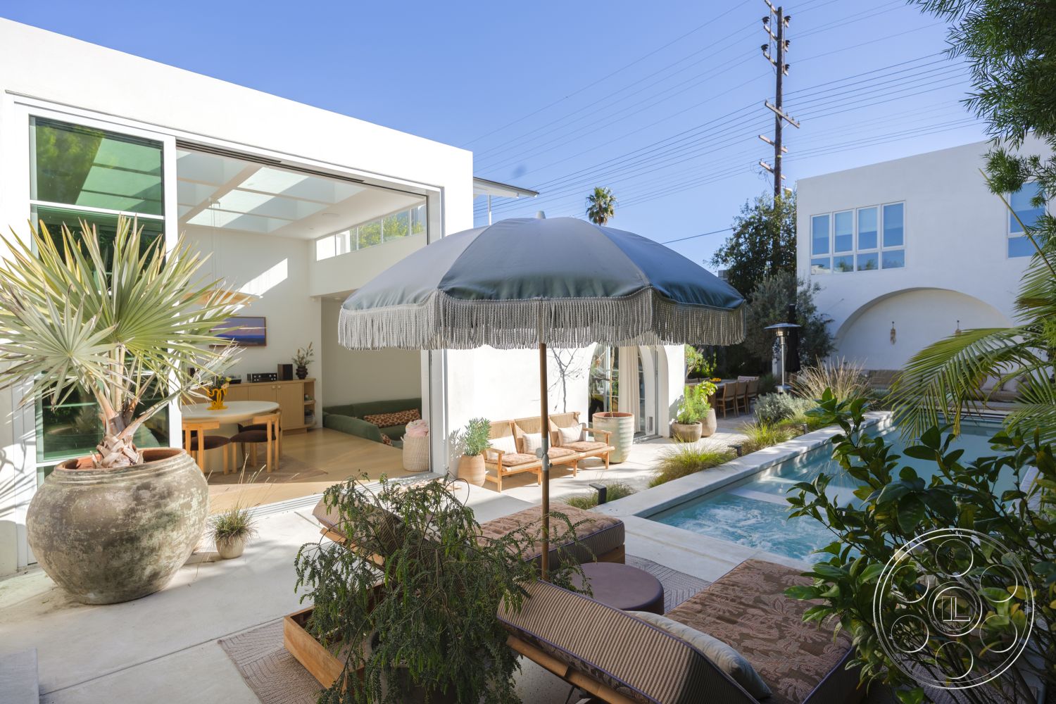 Modern 519 - exterior concrete patio floor, exterior landscaped garden, exterior modern architectural style, exterior glass sliding doors, exterior outdoor lounge area, exterior potted succulents, interior wood dining table, interior light-filled space, exterior rectangular swimming pool, exterior fiberglass umbrella with fringe, exterior stone planter with tropical plants, interior open-concept kitchen and dining area, interior green upholstered seating