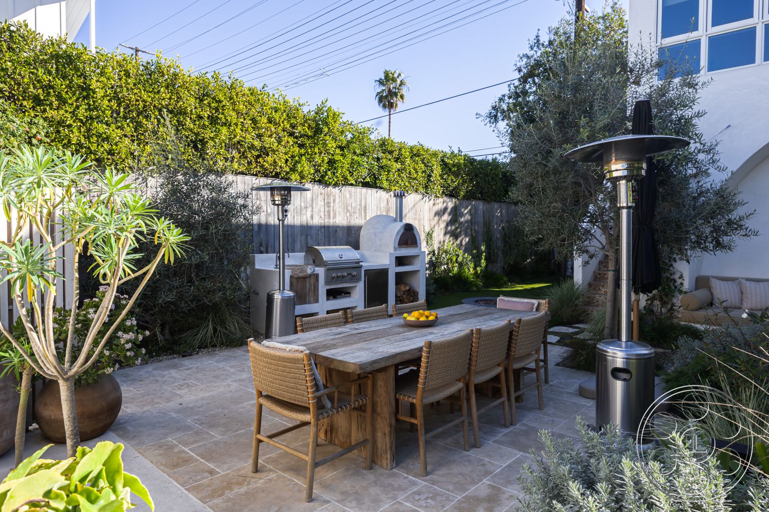 Modern 519 - landscaped garden beds, natural stone patio flooring, decorative planter pots, contemporary outdoor kitchen, sloped garden design, outdoor seating area with cushions, modern outdoor heater, exterior dining patio, wood outdoor dining table, woven rattan dining chairs, stainless steel barbecue grill, exposed stone pizza oven, hardscape fire pit area, privacy fence with wood paneling, tropical plants and greenery, sunny urban garden patio, interior and exterior connection, al fresco dining space, palms and flowering shrubs