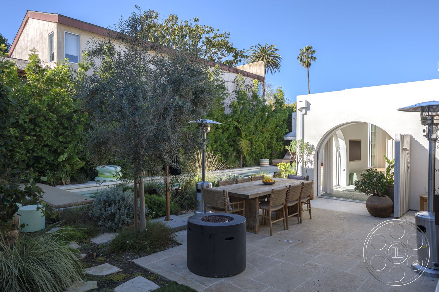 Modern 519 - white stucco walls, rectangular swimming pool, arched entryway, contemporary outdoor space, modern outdoor dining area, sunny outdoor environment, tropical landscaping with palm trees, exterior patio with natural stone flooring, wood dining table with woven chairs, decorative garden planter, outdoor patio heaters, lush greenery surrounding the pool area, casual backyard setting, urban residential home, al fresco dining experience