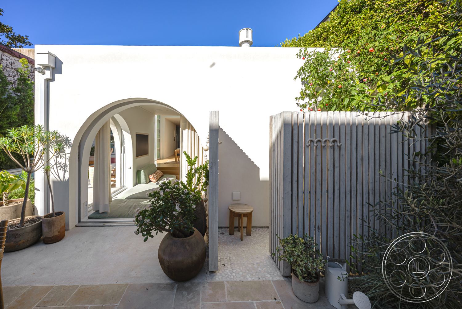 Modern 519 - white stucco walls, floor-to-ceiling windows, wooden slatted fence, arched entryway, modern outdoor setting, potted greenery accents, exterior concrete patio flooring, urban residential environment, round planters with tropical plants, polished stone walkway, bordered garden area, interior bright living area, minimalist design with natural light, contemporary courtyard