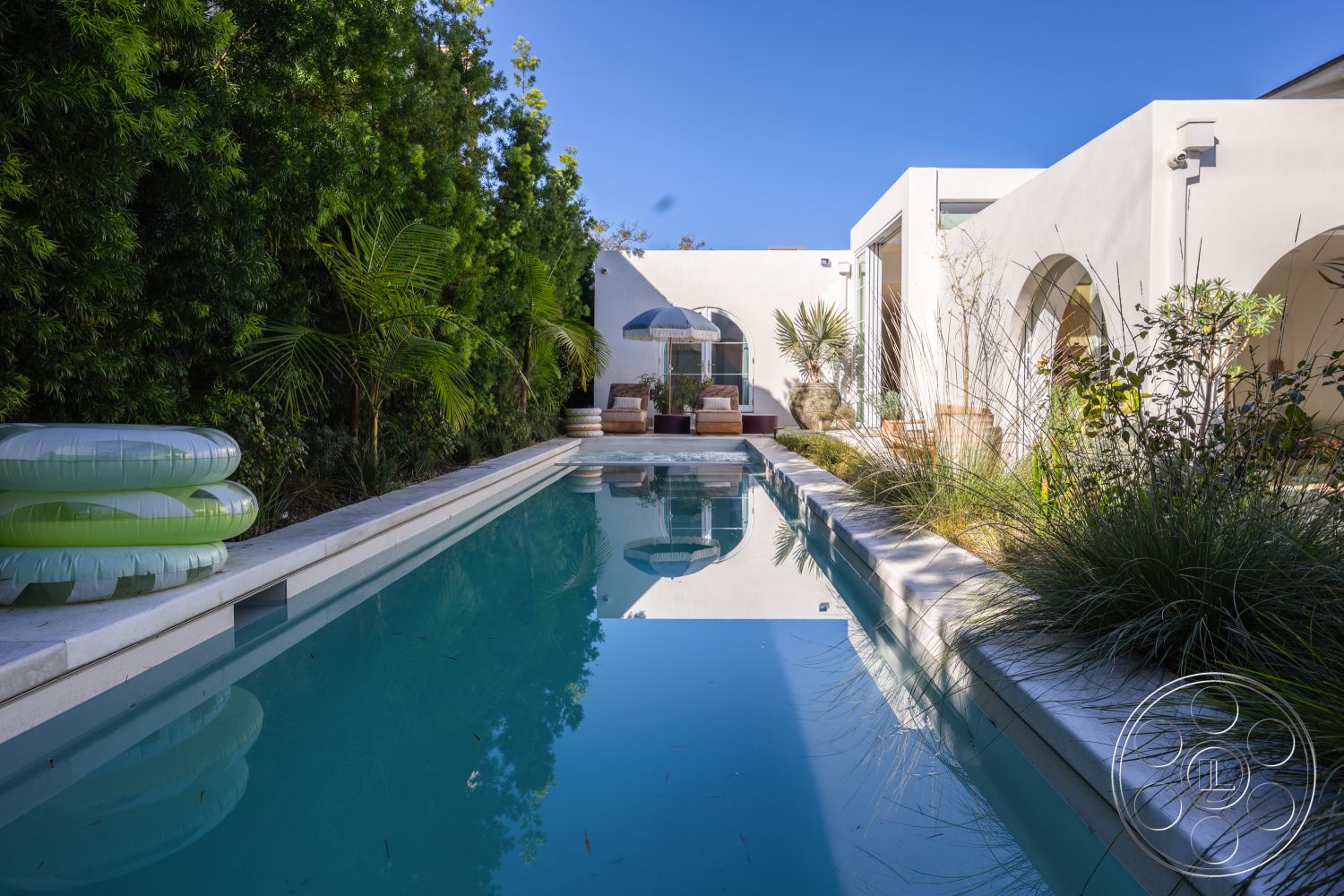 Modern 519 - white stucco walls, outdoor seating area, modern architectural style, clear blue sky, sunshade umbrella, rectangular pool, minimalist landscaping, natural light exposure, concrete pool border, exterior pool area, palm tree accents, arched window design, light-colored stone pavers, surrounding lush vegetation, concrete pool decking, green inflatable pool floaties, tranquil outdoor setting