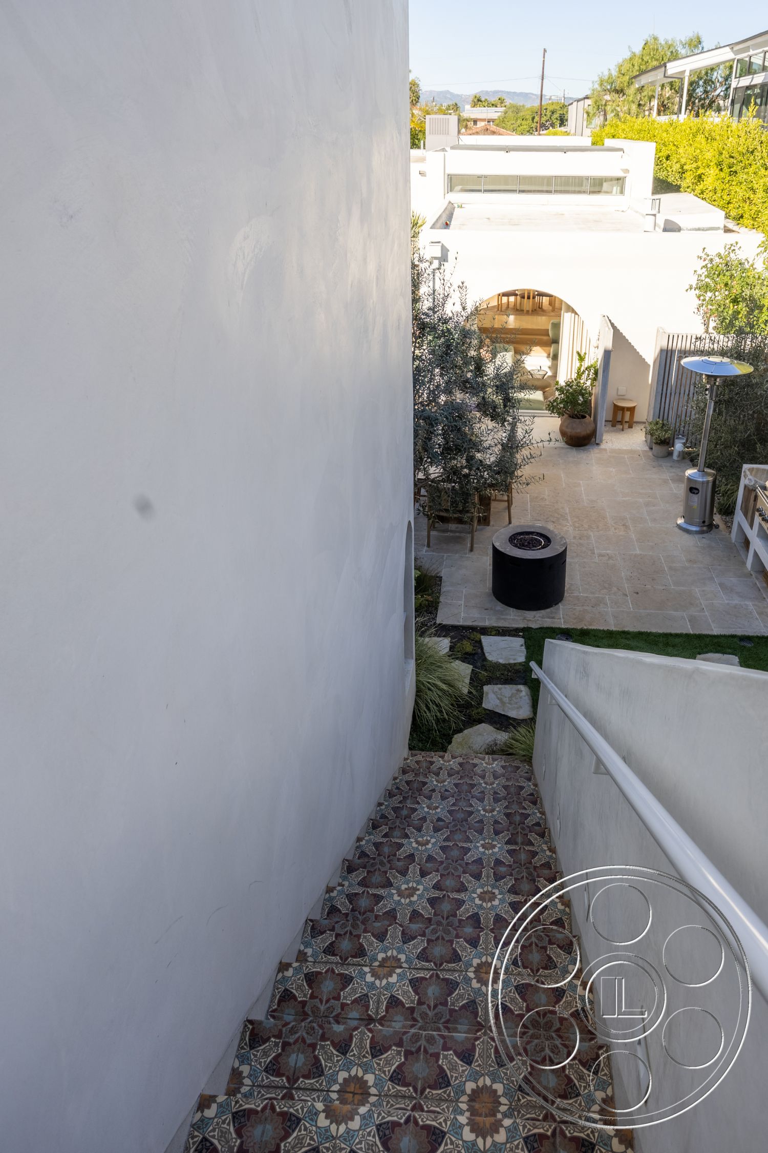 Modern 519 - exterior, landscaped garden, city skyline view, textured plaster walls, courtyard access, glass balcony railing, lush greenery landscape, modern outdoor setting, decorative tile staircase, colorful patterned tile steps, patio area with stone flooring