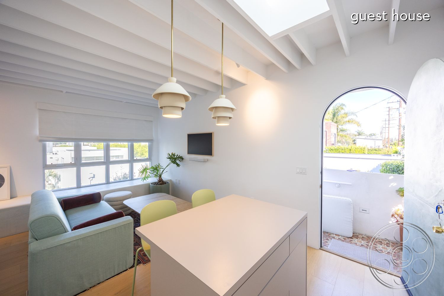 Modern 519 - interior neutral color palette, interior exposed wood ceiling beams, interior large floor-to-ceiling windows, interior soft natural lighting, interior textured area rug, exterior garden patio, interior hardwood living room flooring, interior quartz kitchen countertop, interior white shiplap walls, interior round pendant lighting, interior curved arch doorway, interior modern green sectional sofa, interior minimalist dining table, interior indoor potted plants, interior living room seating area