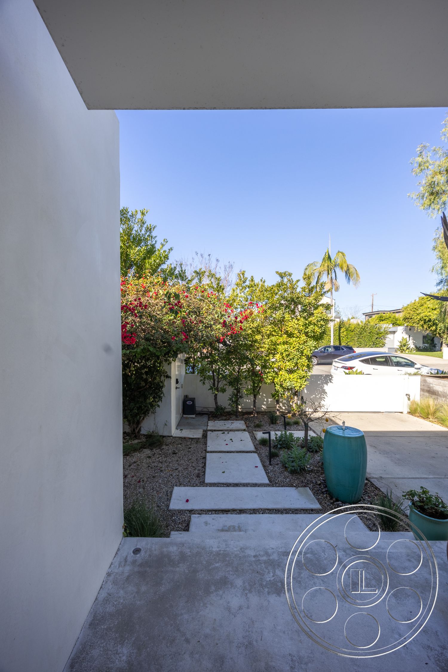 Modern 519 - gravel landscaping, surrounding urban environment, clear blue sky view, modern home entrance, concrete porch steps, smooth white plaster walls, tropical landscaping with palm trees, exterior pathway with concrete stepping stones, vertical plantings with flowering shrubs, modern minimalist entryway, decorative blue water feature, greenery accentuating entrance, lawn border with low maintenance plants