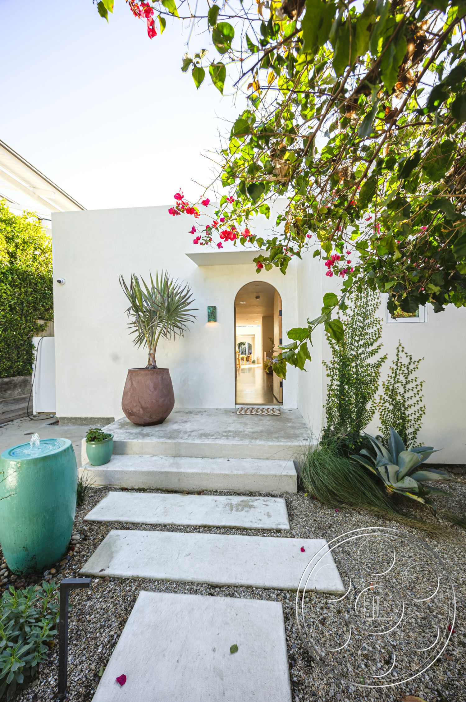Modern 519 - exterior, modern entryway, green foliage, concrete steps, gravel landscaping, stucco walls, arched doorway, landscape design elements, outdoor garden setting, minimalist exterior design, tropical plant accents, natural light entry, rectangular concrete pavers, ceramic flower pots, wooden patio area, door rug at entry, sandstone gravel bed