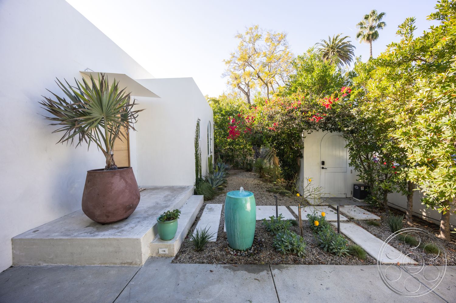 Modern 519 - cobblestone pathway, gravel ground cover, modern minimalist design, exterior white stucco walls, urban garden setting, tropical palm landscaping, rectangular concrete patio, concrete steps leading to entrance, lush flowering plants, decorative ceramic planter, green grasses and shrubs, white wooden garden door, textured concrete borders, curvilinear garden layout, California-style home exterior