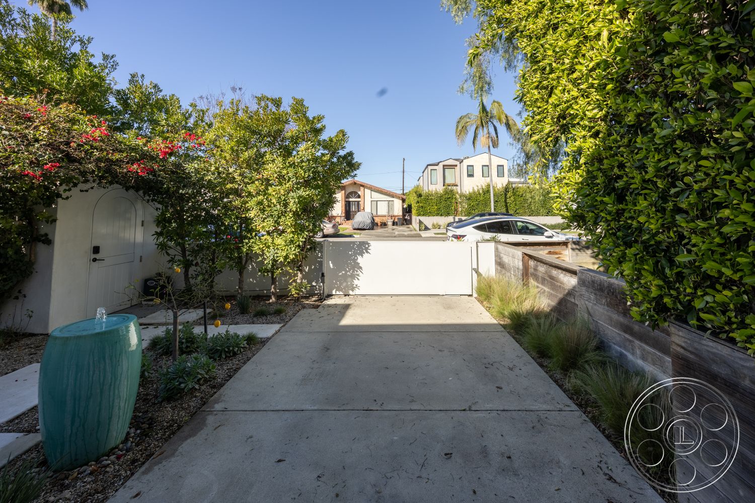 Modern 519 - exterior, white stucco walls, suburban neighborhood, paved walkway, concrete driveway, lush garden landscaping, stone garden accents, modern home entryway, exposed wood fence, custom garden fountain, tropical plant setting