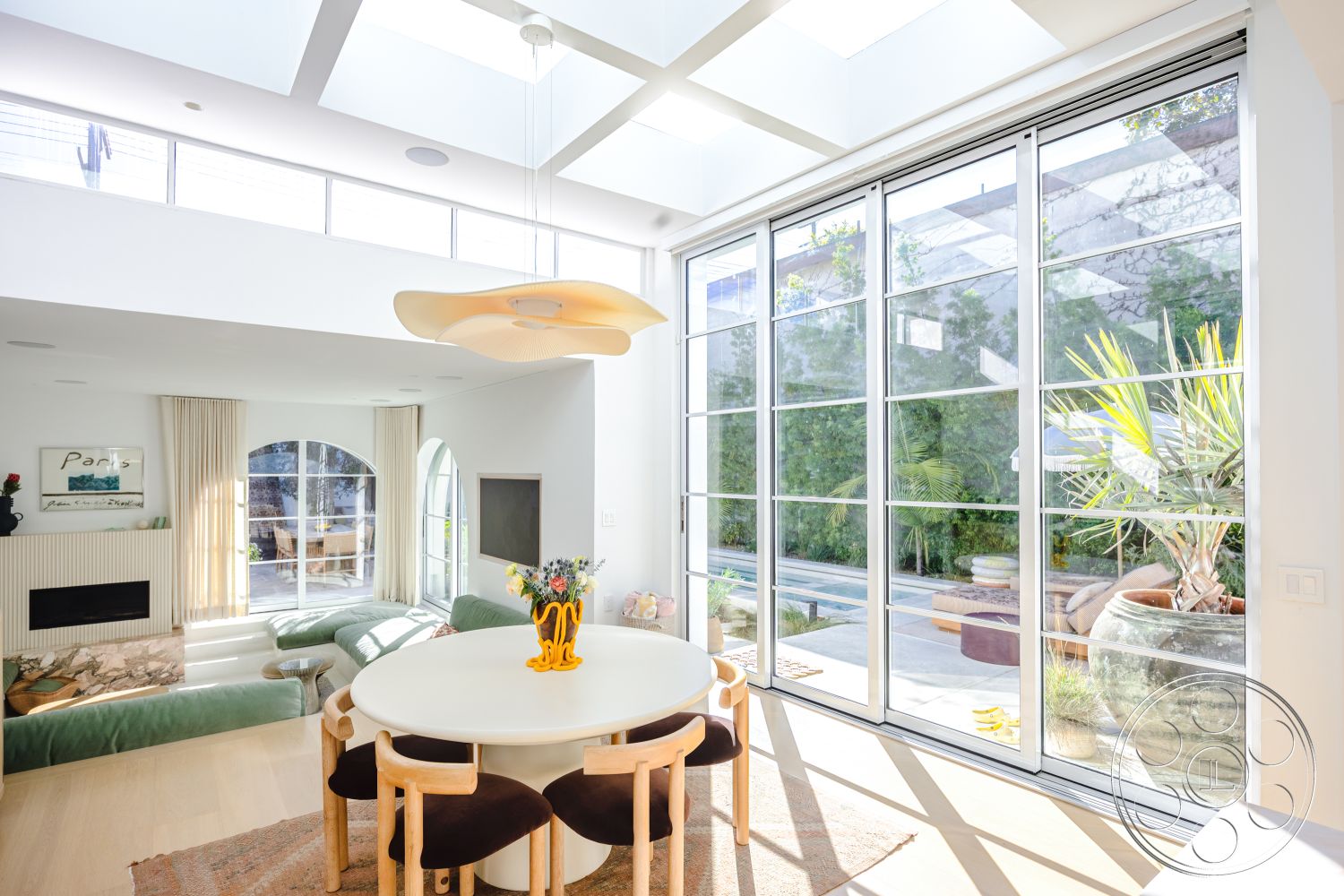 Modern 519 - neutral color palette, light wood flooring, modern pendant lighting, textured wall panels, natural light-filled space, white painted walls, floor-to-ceiling glass sliding doors, minimalist decor with potted plants, vaulted ceiling with skylights, interior bright open living space, built-in low seating area, rounded window shapes, elegant round dining table, black dining chairs with wooden accents, cozy living room area with sofa, airy indoor environment