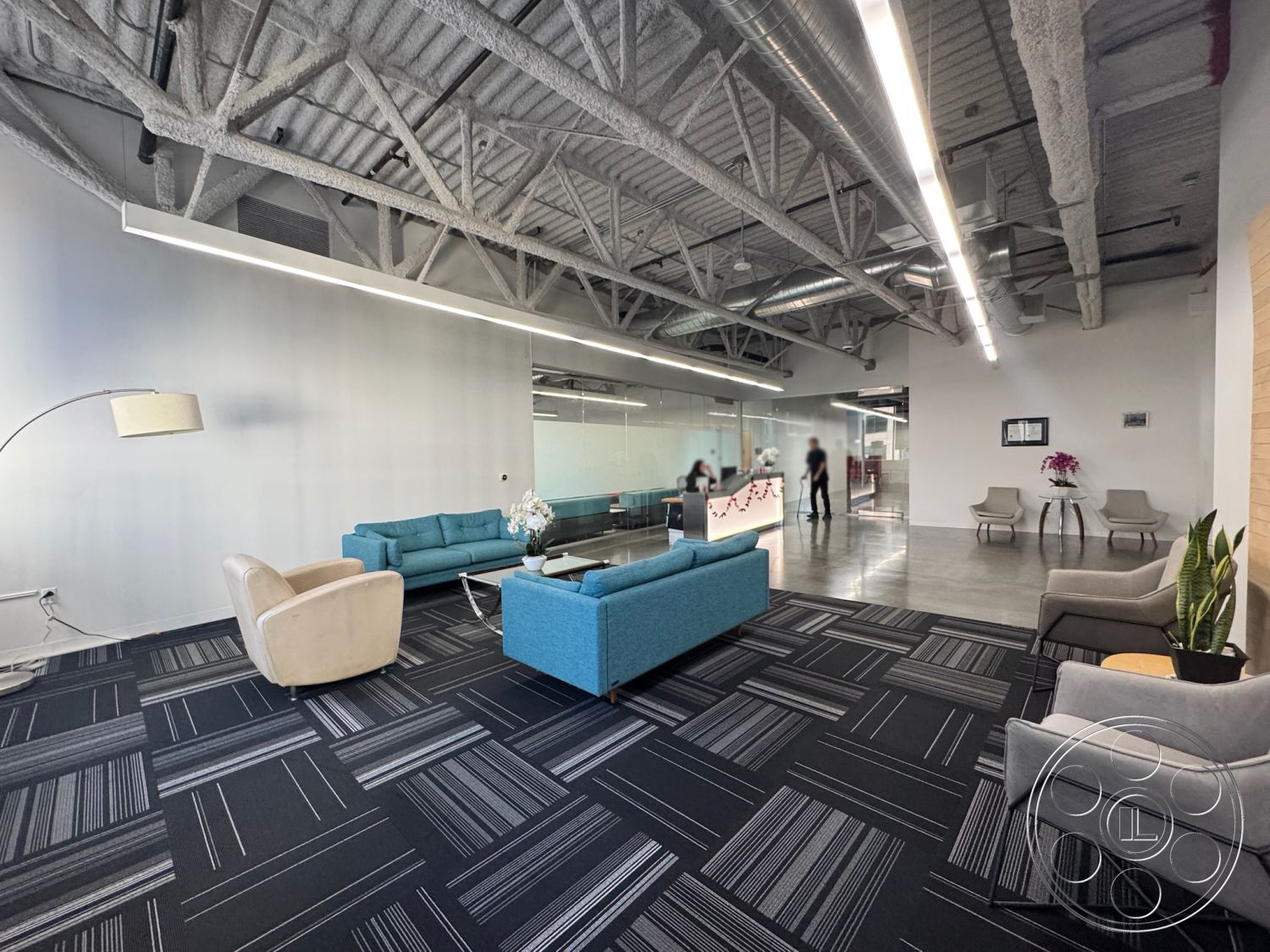 Office 128 - open floor plan, polished concrete flooring, collaborative workspace, blue fabric sofa, glass partition walls, minimalist interior design, contemporary reception area, modular carpet tiles, track lighting fixtures, urban office setting, industrial architectural style, bright white painted walls, exposed steel ceiling beams, light gray armchairs, metal reception desk, small potted plants for decor