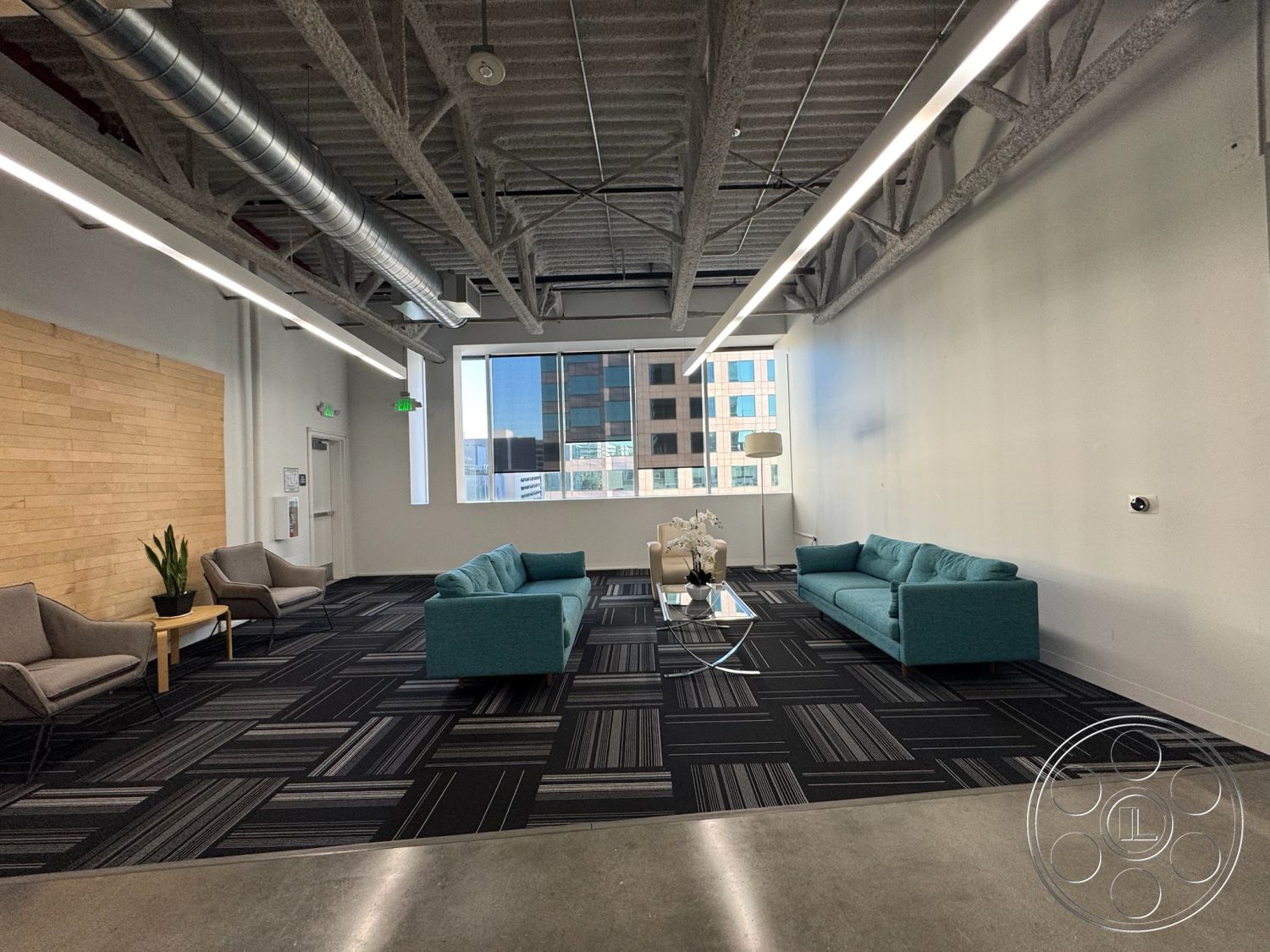 Office 128 - minimalist decor, natural light, open floor plan, glass coffee table, exposed metal beams, sliding glass windows, light wood accent wall, urban office setting, textured ceiling panels, light gray painted walls, striped carpet flooring, plush teal sectional sofa, modern armchairs with metal legs