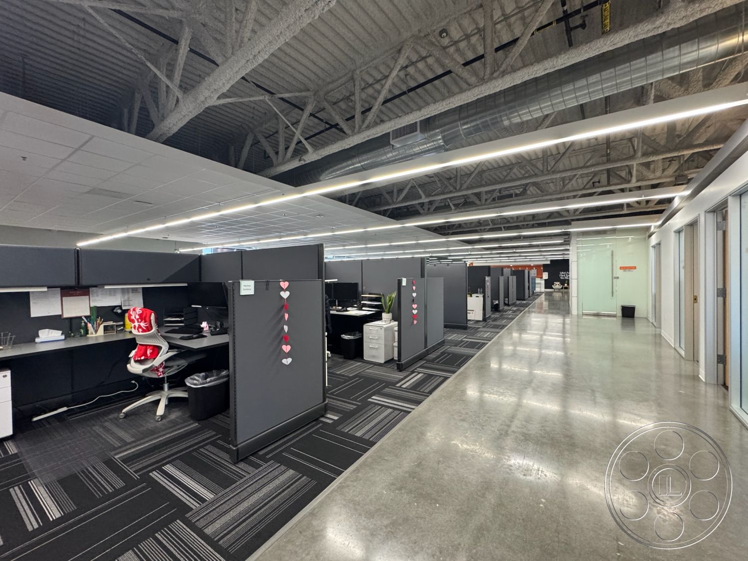 Office 128 - polished concrete flooring, modern office design, functional office space, striped carpet tiles, exposed metal ceiling beams, collaborative workstations, glass entry doors, modular gray cubicles, square glass partition walls, task chairs with ergonomic design, LED linear lighting fixtures, large open workspace layout, industrial-style office interior, dark gray office walls, elegant office environment