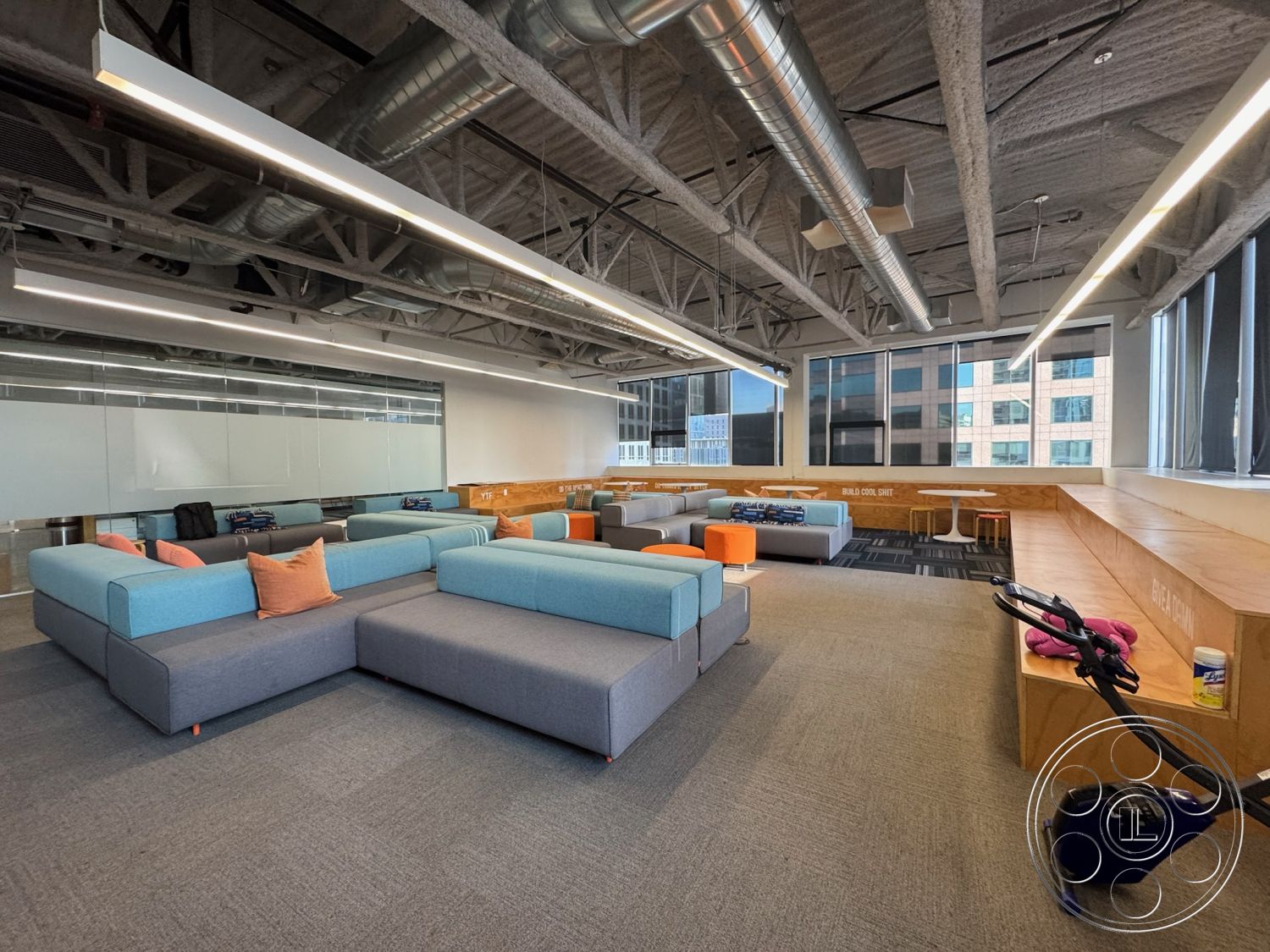 Office 128 - creative workspace, minimalist design elements, textured plaster ceiling, light wood paneling, exposed steel beams, gray upholstered furniture, collaborative work area, interior office space, large windows with city view, black carpet tiles, flexible seating layout, open ceiling design, modular seating arrangement, soft upholstery lounge seating, bright accent pillows, wooden built-in benches, low-profile modern tables, overhead LED lighting