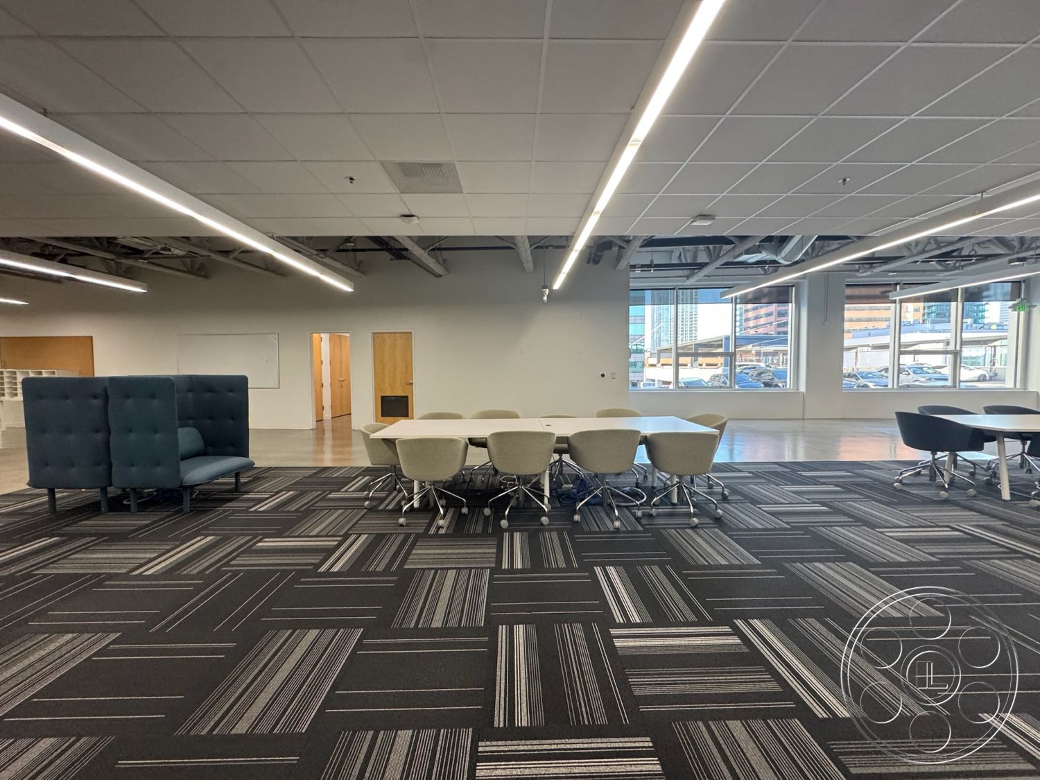 Office 128 - wooden doors, exposed ceiling beams, open-plan layout, collaborative work area, LED lighting fixtures, interior office space, large windows with city view, flexible seating arrangement, whiteboard wall, carpet tile flooring, concrete polished flooring, modern task chairs, round conference table, soft seating area with blue upholstery, commercial workspace, acoustical furniture partition