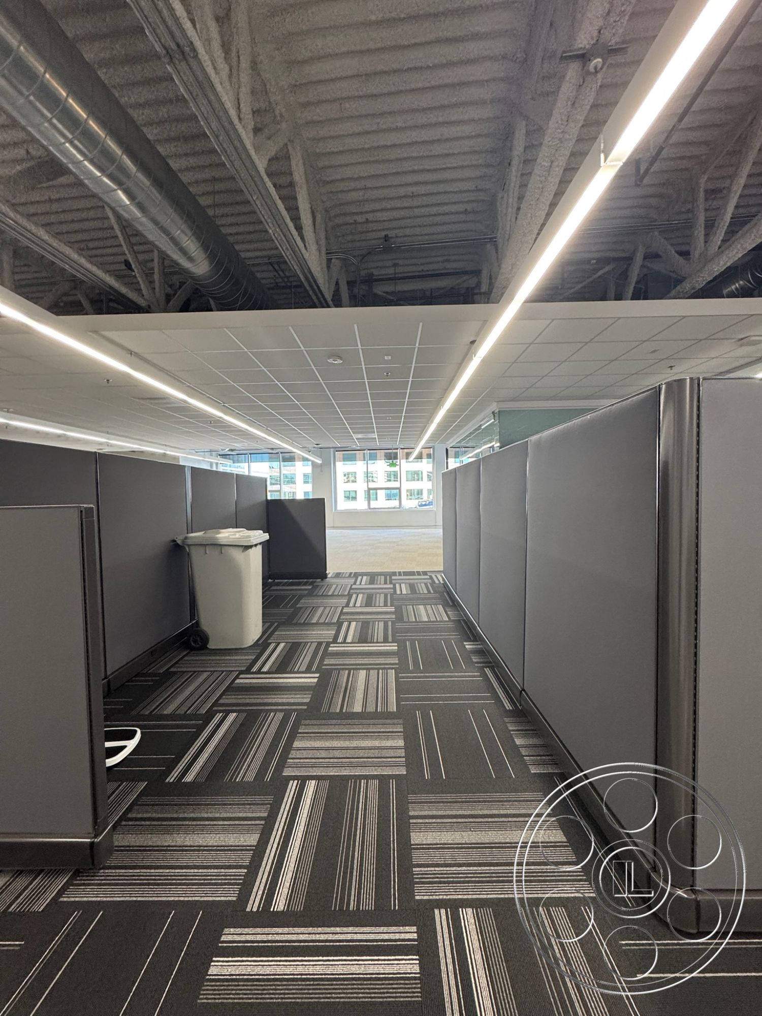 Office 128 - minimalist decor, open floor plan, functional workspace, floor-to-ceiling windows, collaborative environment, linear light fixtures, modern office design, interior office space, striped carpet tiles, industrial-style lighting fixtures, cohesive color palette, acoustic tile ceiling, exposed metal ductwork, cubicle workstation layout, neutral gray cubicle walls, potato bin trash can