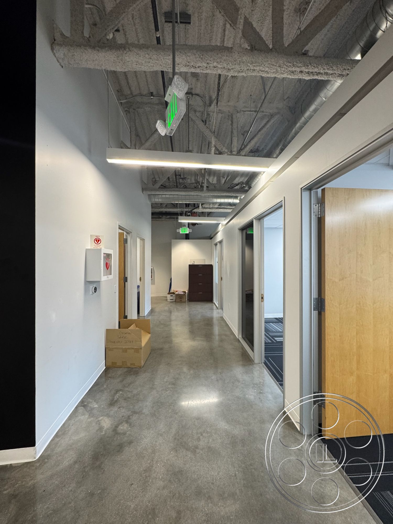 Office 128 - neutral color palette, textured plaster walls, black accent wall, open office layout, acoustic ceiling tiles, modern minimalist design, commercial office space, industrial style architecture, glass office partition walls, exposed concrete hallway floor, drop ceiling with exposed ductwork, light wood door frames, interior corridor lighting, straight corridor, stainless steel overhead fixtures