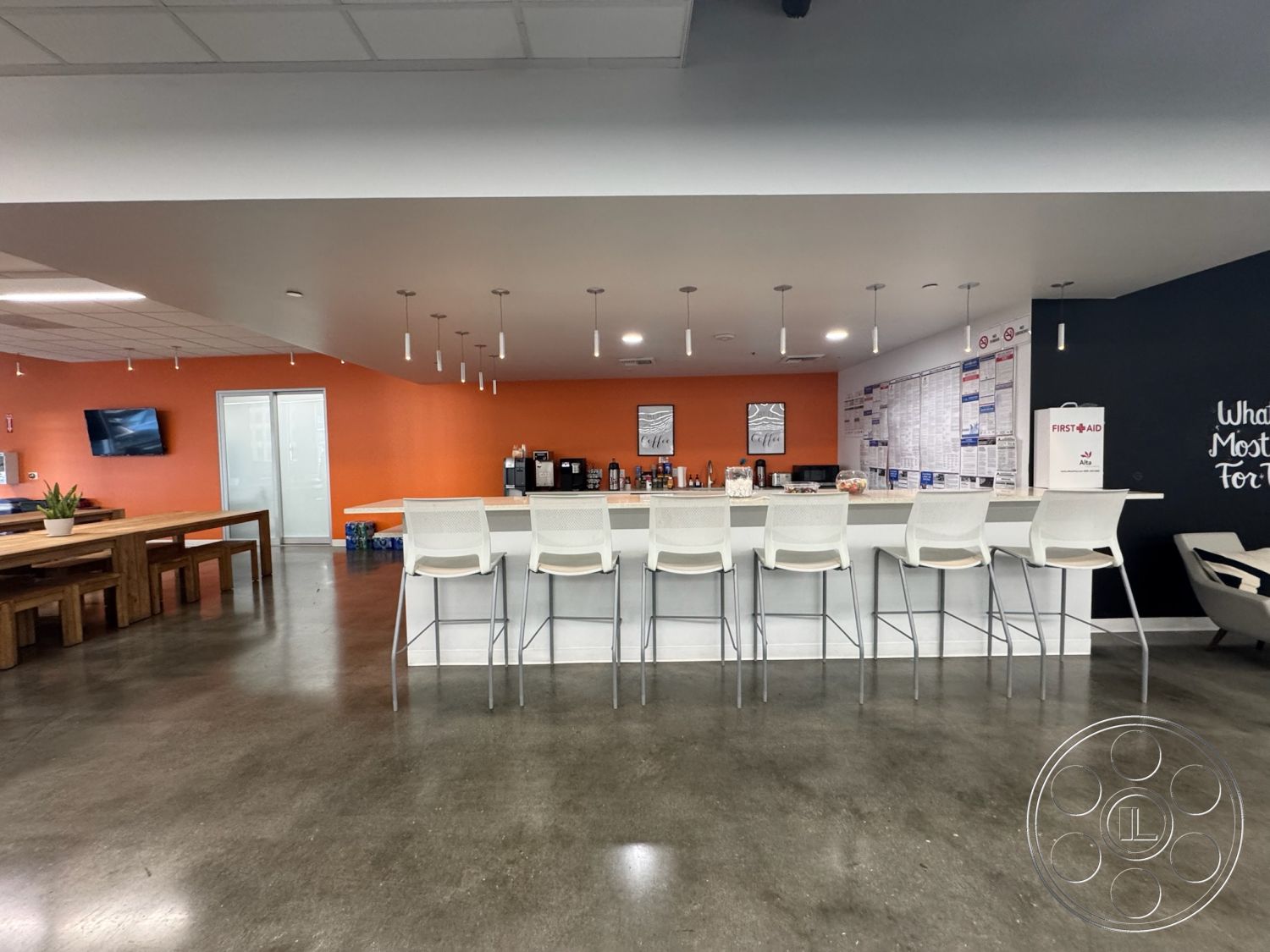 Office 128 - minimalist design, polished concrete floor, wooden dining table, interior space, collaborative workspace, decorative indoor plant, orange accent wall, metal pendant lighting, glass door entrance, informal meeting area, modern wall art, stylish lounge chair, black chalkboard wall, white bar stools, open-plan kitchen area, modern bar countertop, functional kitchen appliances