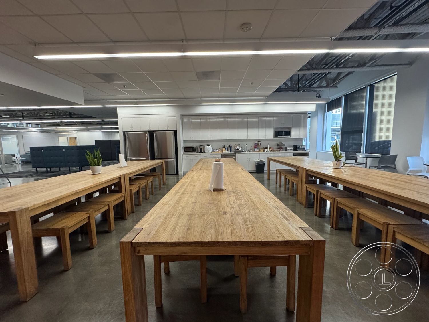 Office 128 - neutral color palette, polished concrete flooring, modern lighting fixtures, stainless steel kitchen appliances, minimalist interior decor, urban office setting, large windows providing natural light, contemporary seating arrangement, functional workspace design, industrial kitchen interior, exposed ceiling ducts, modern wooden communal tables, oak wood table tops, simple wooden bench seating, white cabinetry with minimal hardware, open plan office concept