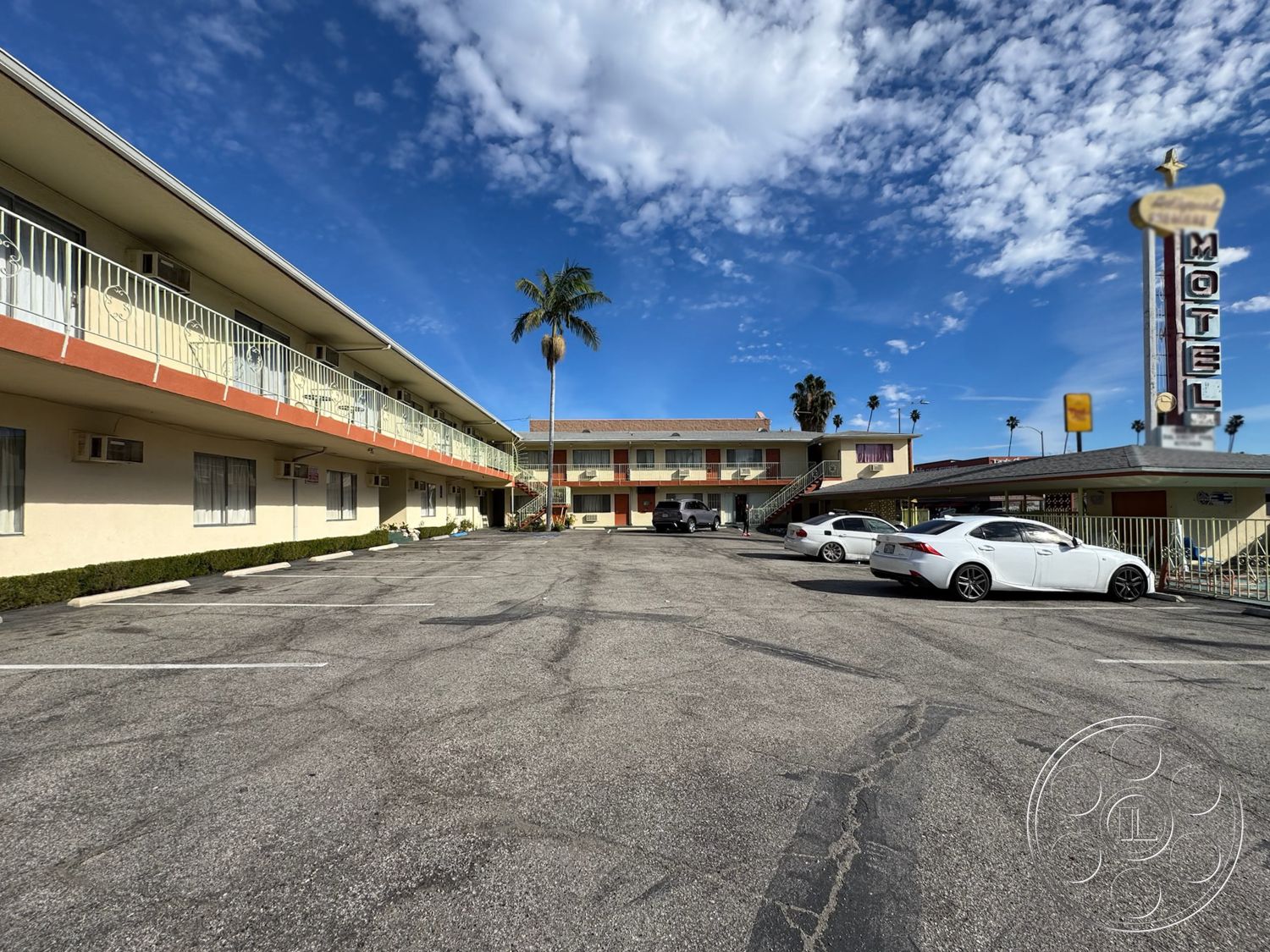 Hotel 59 - exterior, outdoor seating area, paved parking lot, flat roof design, palm tree landscaping, brick driveway pavers, city skyline backdrop, motel facade, retro motel sign, stucco building exterior, balcony railing detail, aluminum siding elements, landscaped green shrubs, horizontal building layout, second-story balconies, concrete pedestrian pathway, curved edge driveway, air conditioning units on walls