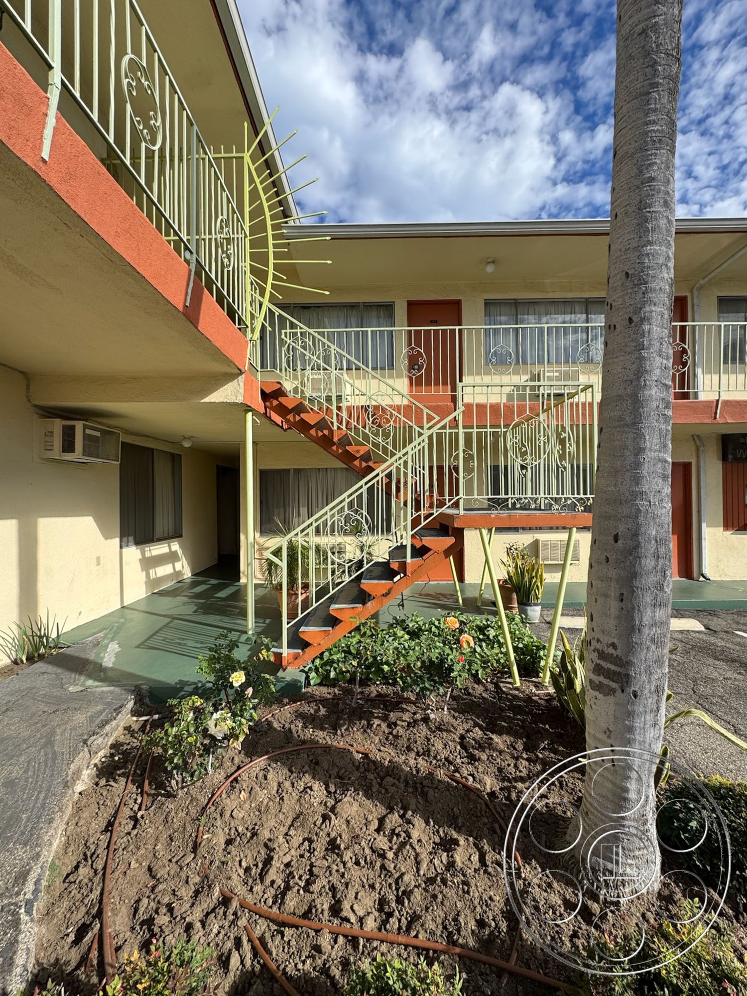 Hotel 59 - exterior concrete patio floor, exterior recessed lighting, palm tree landscaping, exterior colorful flower beds, exterior painted stucco walls, exterior metal railing staircase, exterior wrought iron stair railings, exterior curved staircase, exterior desert garden plantings, exterior asphalt pathway, exterior residential courtyard, exterior vintage motel architecture, exterior sunburst architectural detail, exterior green door accents, exterior white window frames