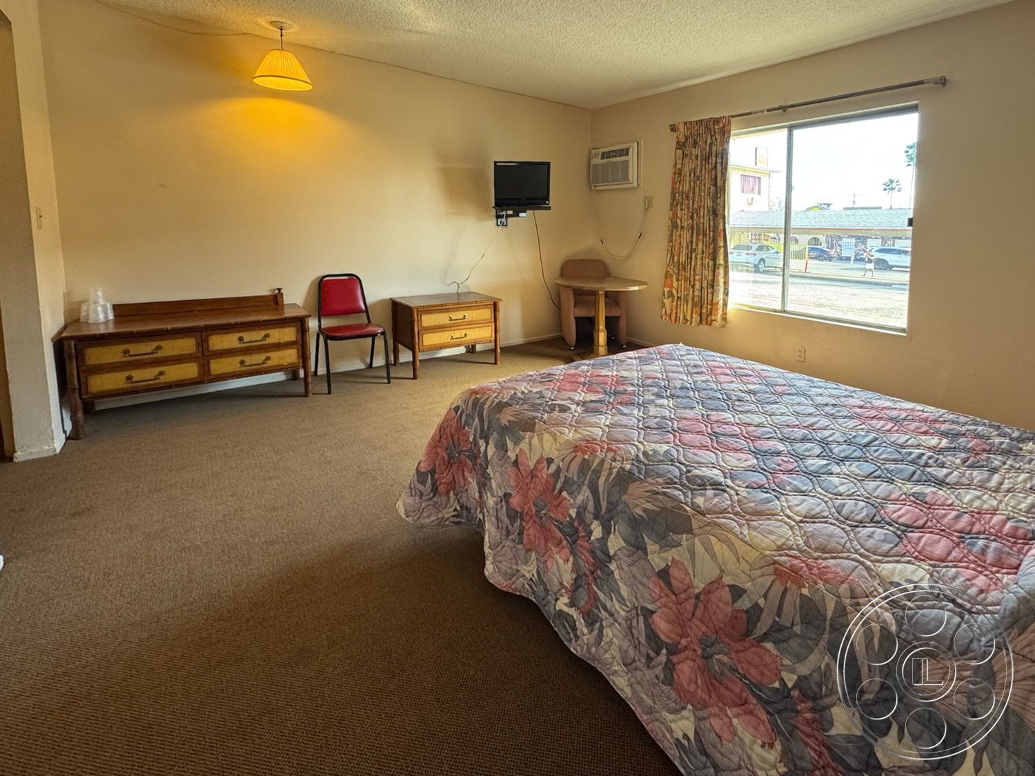 Hotel 59 - bright natural light, wooden dresser, simple decor, exterior view, upholstered chair, neutral wall color, flat-screen television, carpet bedroom flooring, floral patterned bedspread, lampshade ceiling light fixture, window with curtain, corner table, casual hotel room