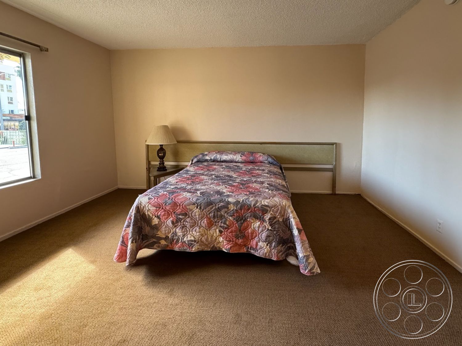 Hotel 59 - neutral wall color, textured plaster walls, natural light from window, low-profile furniture, single-pane windows, carpet bedroom flooring, rural farmhouse style, lampshade table lamp, queen-size bed with floral quilt, simple headboard design, open bedroom layout