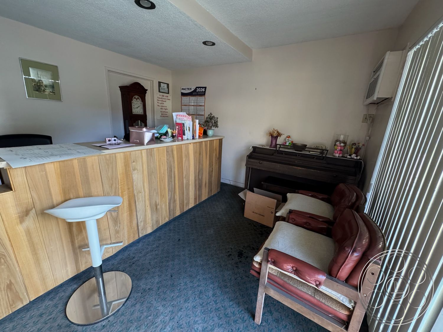 Hotel 59 - minimalist decor, textured ceiling, framed wall art, wooden clock, natural light from window, carpet office flooring, wood panel reception desk, office reception area, wall-mounted air conditioning unit, upholstered vintage leather chairs, piano against the wall, decorative display items, bright office lighting, box storage