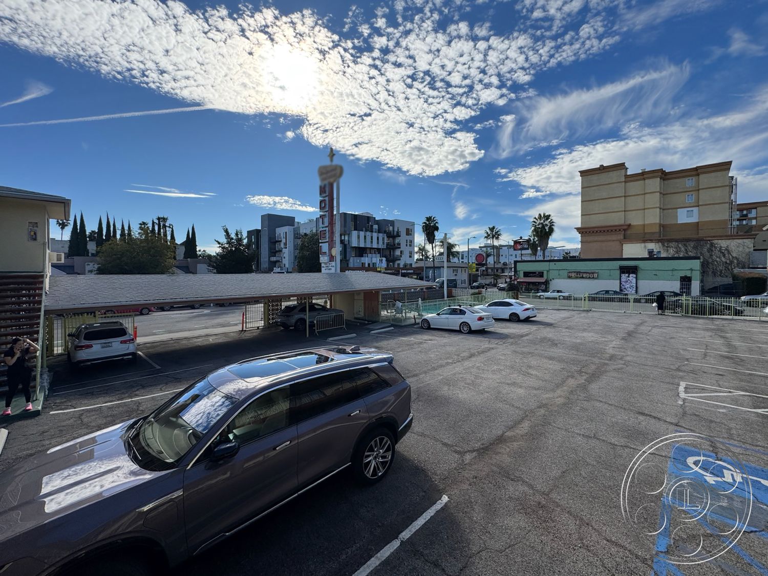 Hotel 59 - city view, outdoor seating area, metal railing, urban environment, landscaped planters, surrounding palm trees, asphalt parking lot surface, cloudy blue sky, horizontal wooden slat carport design, modern motel signage, two-story hotel structure, paved parking space layout, mixed-use commercial buildings, exterior parking design