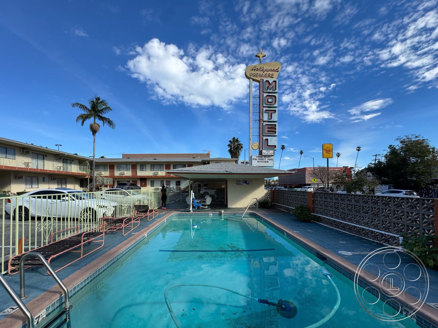 Hotel 59 - exterior, brick landscaping, city skyline view, textured plaster walls, rectangular pool, white painted walls, concrete pool border, palm tree landscaping, tile patio flooring, open courtyard setting, glass pool cleaning equipment, two-story motel, modern motel signage, steel pool railing, hardwood motel lobby floors