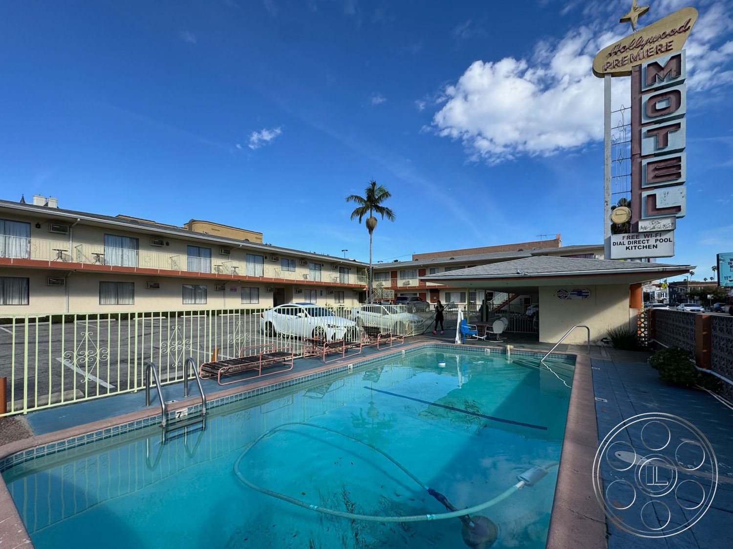 Hotel 59 - exterior, glass sliding doors, outdoor seating area, city skyline view, tropical landscaping, tile roof, concrete pool deck, rectangular pool, paved parking lot, metal staircases, stucco exterior walls, palm tree surroundings, retro motel signage, two-story motel, courtyard-style layout, concrete swimming pool, metal pool fence, acrylic windows, painted wood railings, exposed steel longitudinal beams, distant mountain views