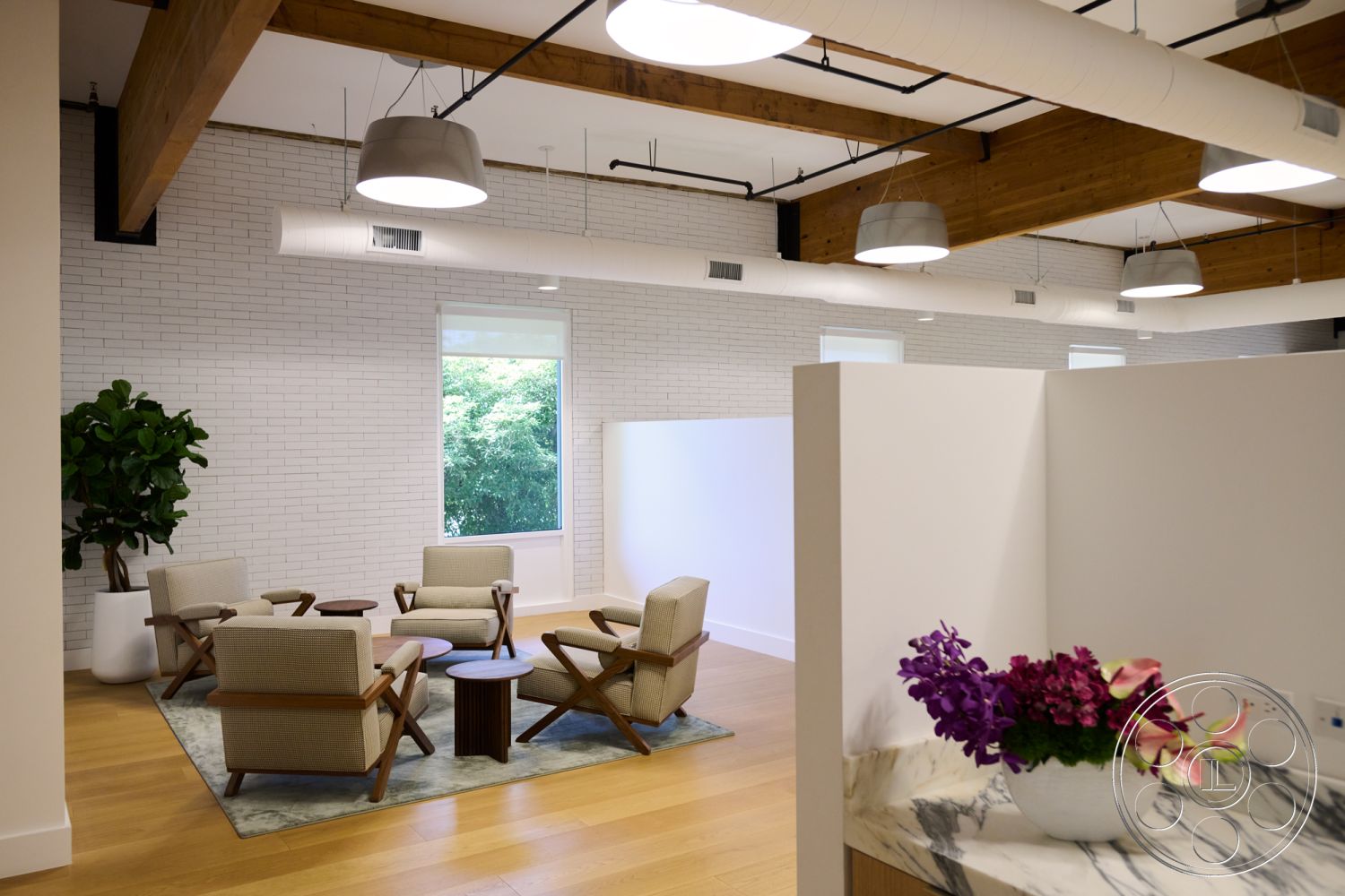 Office 129 - hardwood flooring interior, exposed wood ceiling beams interior, open floor plan interior, natural light-filled space interior, industrial pendant lighting interior, glass partition wall interior, modern lounge seating interior, minimalist decor interior, white painted brick accent wall interior, circular wood coffee table interior, large windows with nature view interior, marble countertop interior, multicolored floral arrangement interior, soft area rug interior