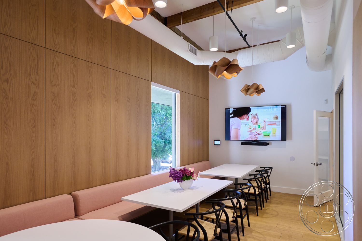 Office 129 - neutral color palette, contemporary design, floor-to-ceiling windows, textured plaster walls, light wood paneling, exposed wood ceiling beams, interior dining area, black metal dining chairs, modern pendant light fixtures, pink upholstered bench seating, round white dining tables, linear ceiling ductwork, multimedia presentation wall, cheerful atmosphere