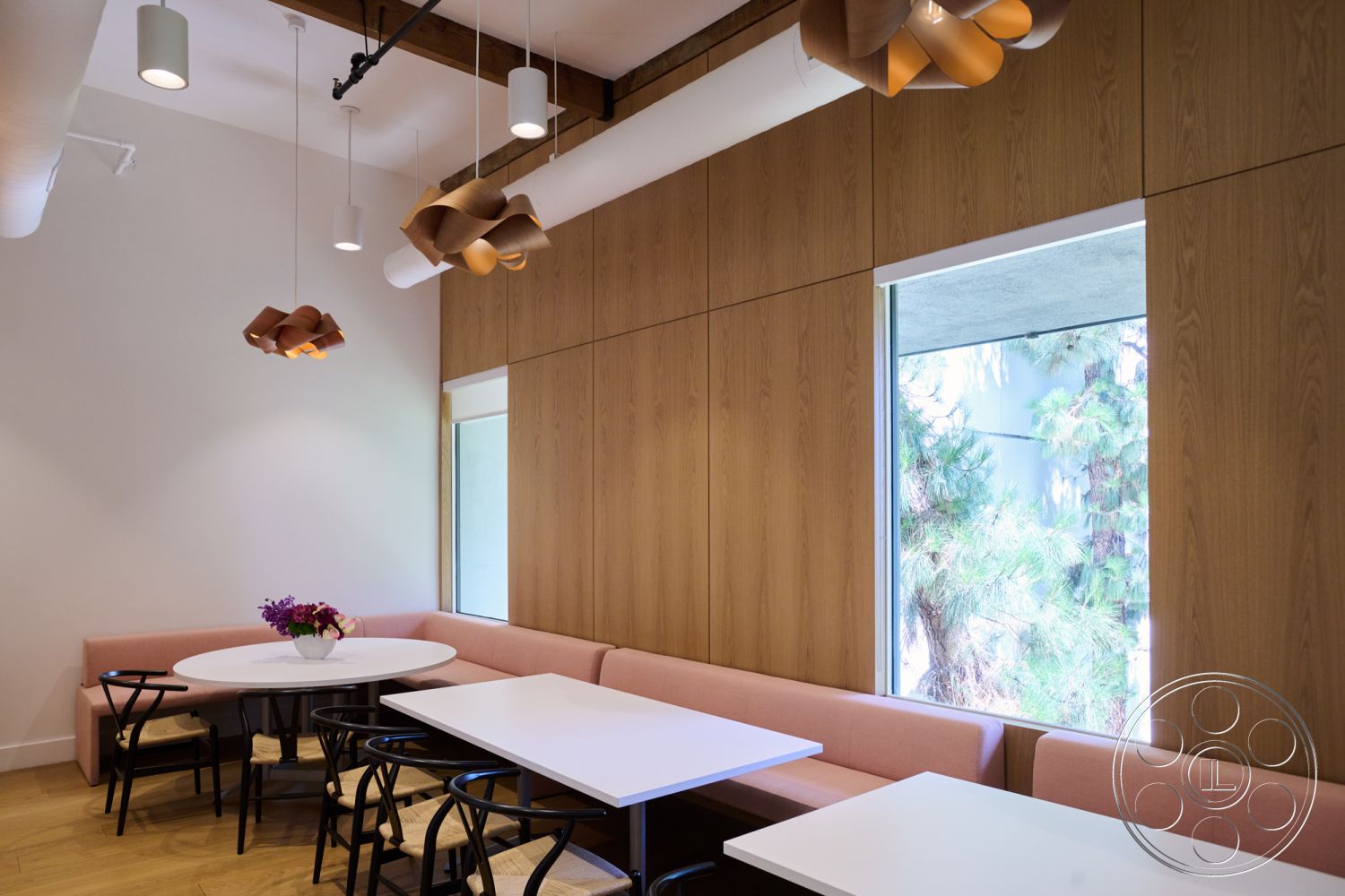 Office 129 - interior wood paneling, interior modern pendant lighting, interior hardwood flooring, interior decorative flower arrangement, interior minimalist design, interior black metal chairs, interior contemporary style, interior open dining area, interior exposed ceiling beams, interior rectangular white tabletops, interior pink upholstered bench seating, interior large window with natural light, interior natural greenery view, interior organic shapes in lighting