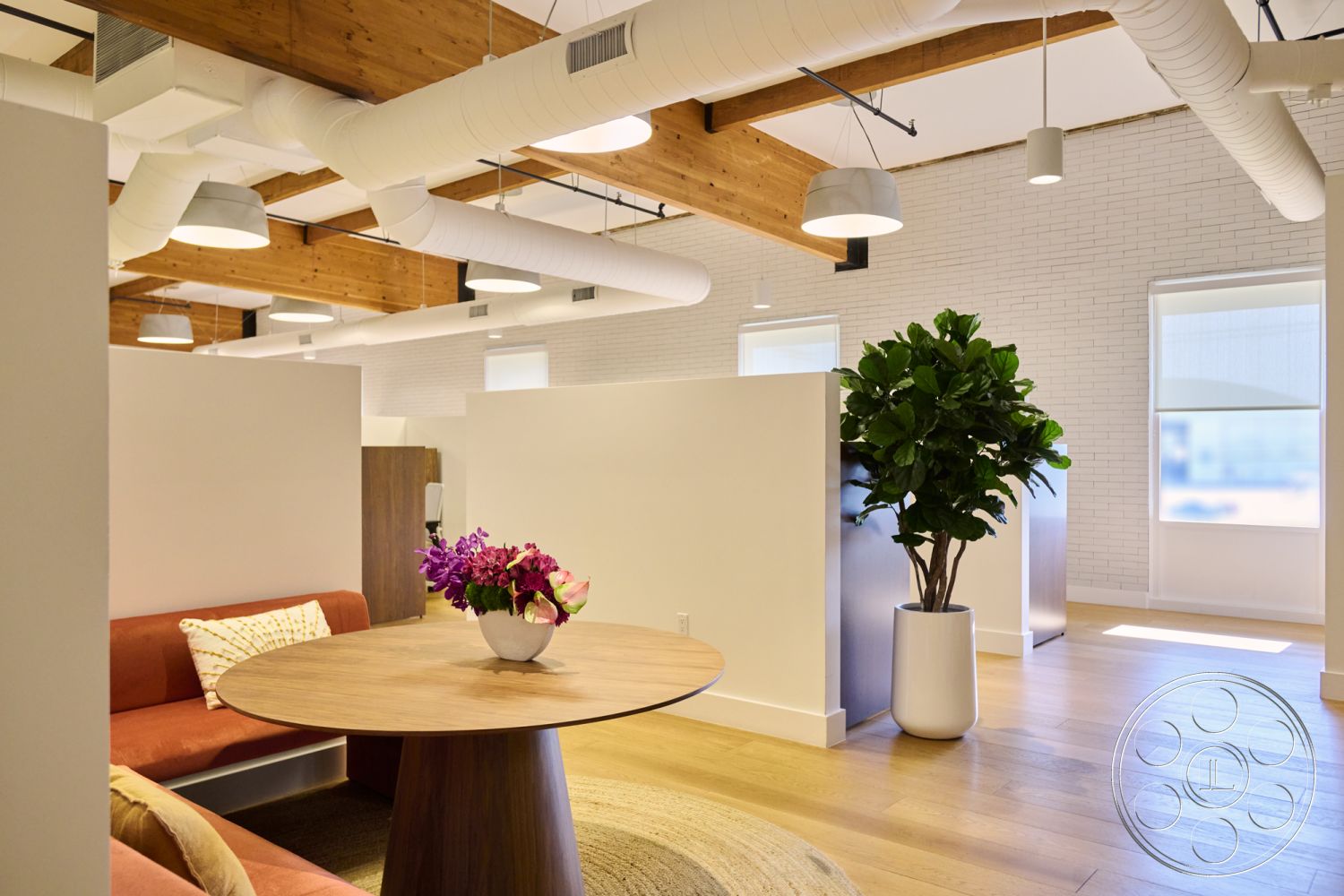 Office 129 - minimalist decor, neutral color palette, hardwood flooring, decorative indoor plant, textured wall treatment, office environment, circular dining table, open office layout, exposed wood ceiling beams, modern lounge seating, natural sunlight exposure, rustic interior design, white painted brick walls, suspended modern light fixtures, cozy meeting space, industrial-style air ducts, workspace with dividers