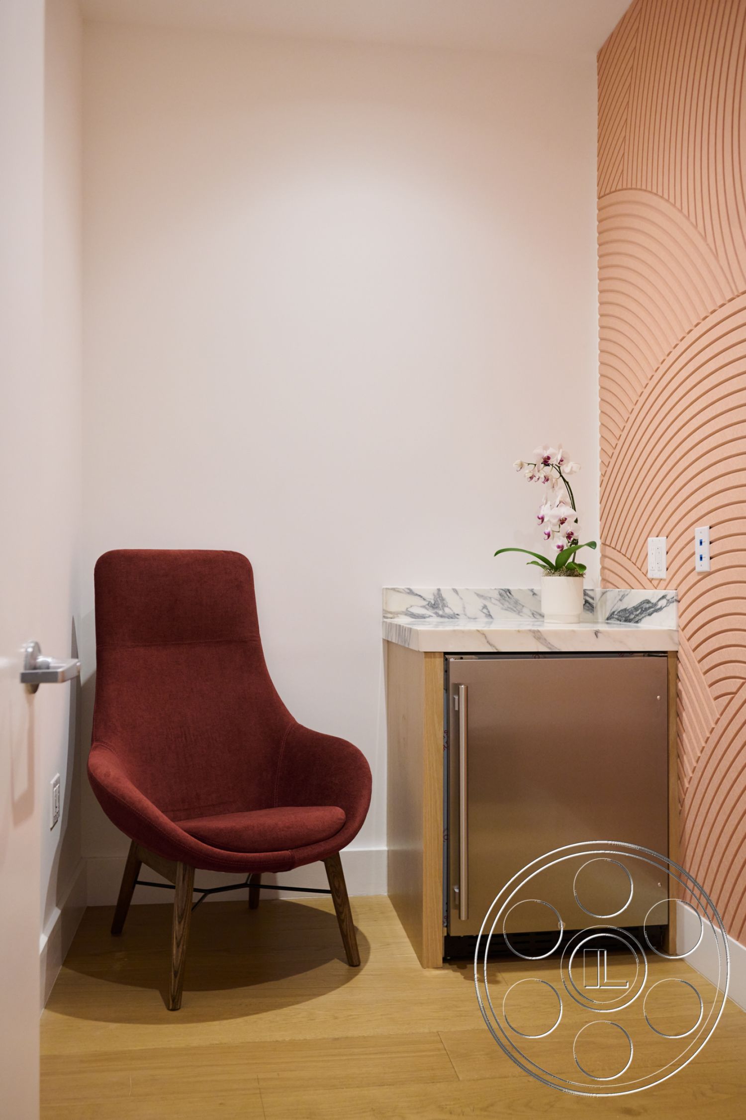 Office 129 - interior space, marble countertop with veining, minimalist design aesthetic, walnut hardwood flooring, white painted walls, indoor plant decoration, contemporary accent chair, rounded chair shape, 3D textured wall treatment, stainless steel mini-fridge, open corner layout