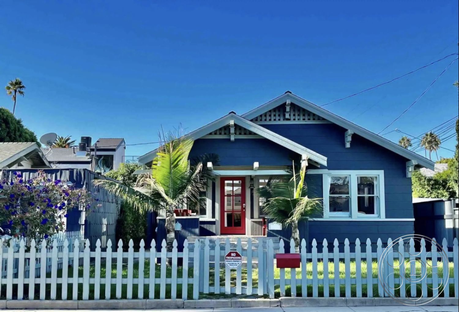 Craftsman 56 - clear blue sky, white picket fence, double-hung windows, blue wood siding exterior, lush green front lawn, arching gable roofline, decorative wood eaves, red front door, bright tropical landscaping, directly adjacent neighboring houses