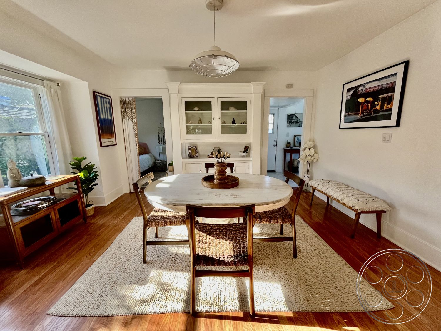 Craftsman 56 - round marble dining table, suburban home setting, exposed wood trim details, large windows with natural light, open layout interior, hardwood dining room floors, textured white plaster walls, cozy dining area, woven rattan dining chairs, neutral wool area rug, mid-century modern dining light fixture, built-in glass-front cabinets, natural greenery decor, soft curtain window treatments