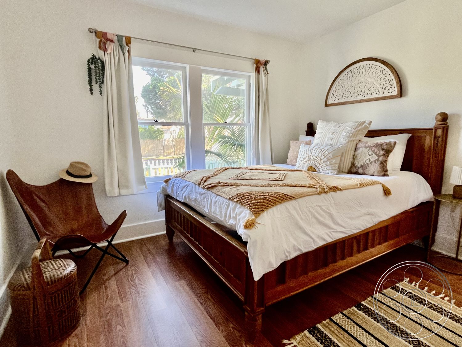 Craftsman 56 - wooden bed frame, natural light from windows, decorative throw pillows, textured wall hanging, interior bedroom, hardwood bedroom floors, white painted walls, tropical garden view, lightweight decorative blanket, curtains with decorative tiebacks, batik patterned area rug, traditional wooden nightstand, comfortable accent chair, woven bamboo storage basket