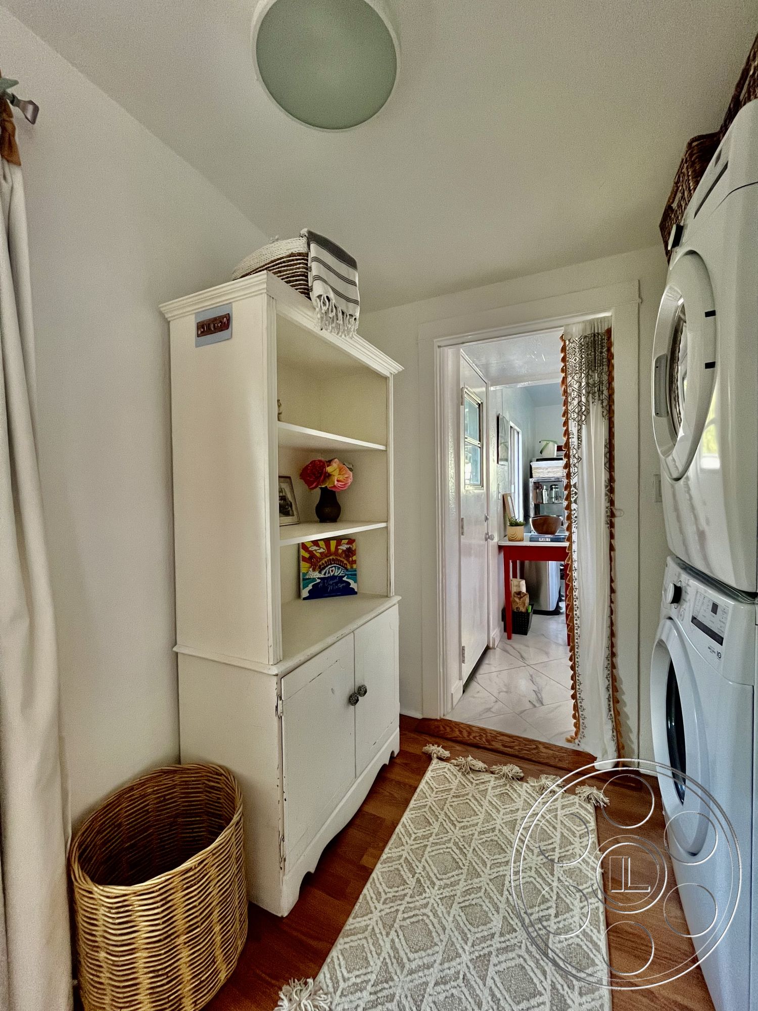 Craftsman 56 - hardwood flooring, textured area rug, decorative wall art, light-filled space, white painted walls, interior laundry room, woven laundry basket, traditional farmhouse style, vintage white wood shelving unit, sconce ceiling light fixture, open doorway to utility room, mirror with decorative trim, functional laundry space