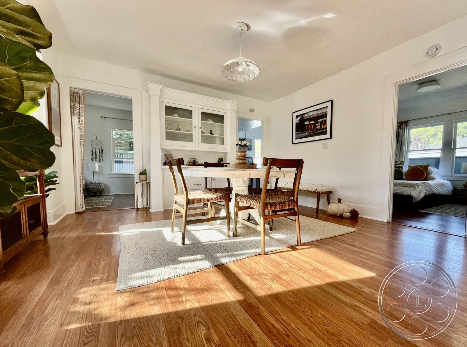 Craftsman 56 - neutral color palette, textured area rug, modern farmhouse style, glass light fixture, exposed wood ceiling beams, white painted walls, interior hardwood dining room floors, dining table with decorative centerpiece, woven seating dining chairs, built-in glass cabinet, light-filled open plan, adjacent living area view