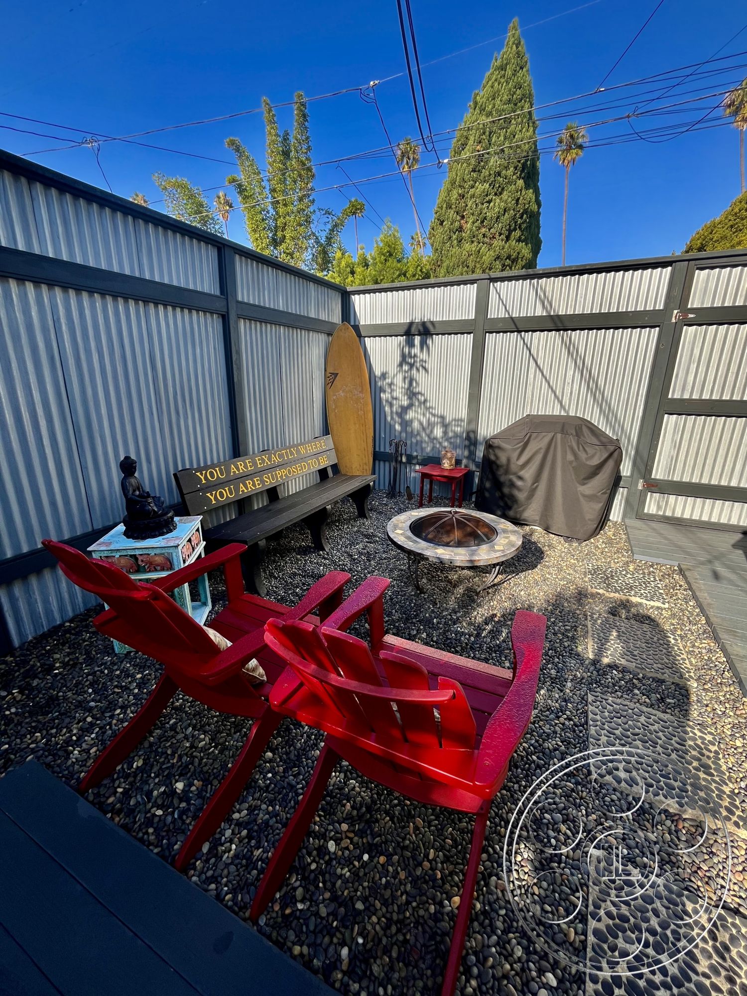 Craftsman 56 - exterior, decorative sculpture, outdoor dining area, outdoor living space, wooden bench seating, privacy fence, palm tree view, tropical landscape setting, cozy fire pit area, pebble stone patio flooring, red adirondack chairs, metal corrugated wall panels, fire pit with circular stone surround, surfer silhouette decoration, textured concrete stepping stones