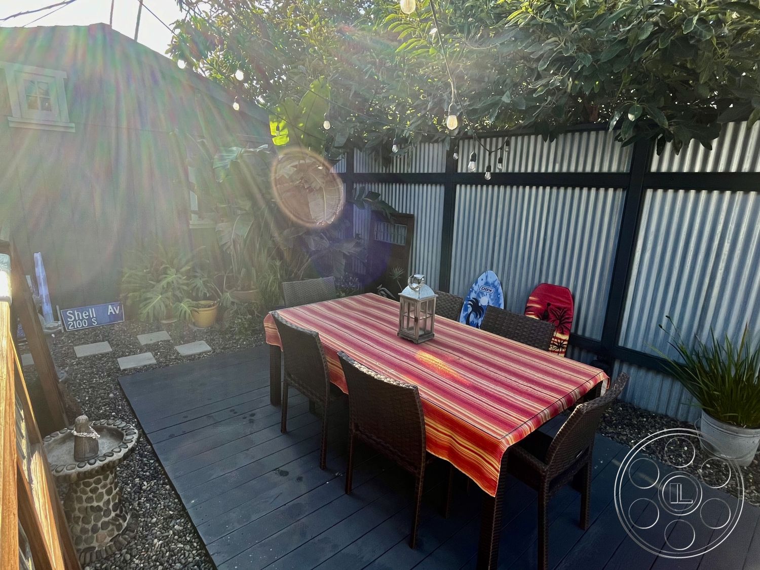 Craftsman 56 - potted plants, outdoor dining area, modern rustic style, corrugated metal wall, stepping stone pathway, landscaped garden setting, wooden deck flooring, outdoor leisure space, sunlit exterior space, woven wicker dining chairs, striped tablecloth, decorative outdoor lantern, metal fence panels, exposed aggregate stone, string lights for ambience, green foliage overhead