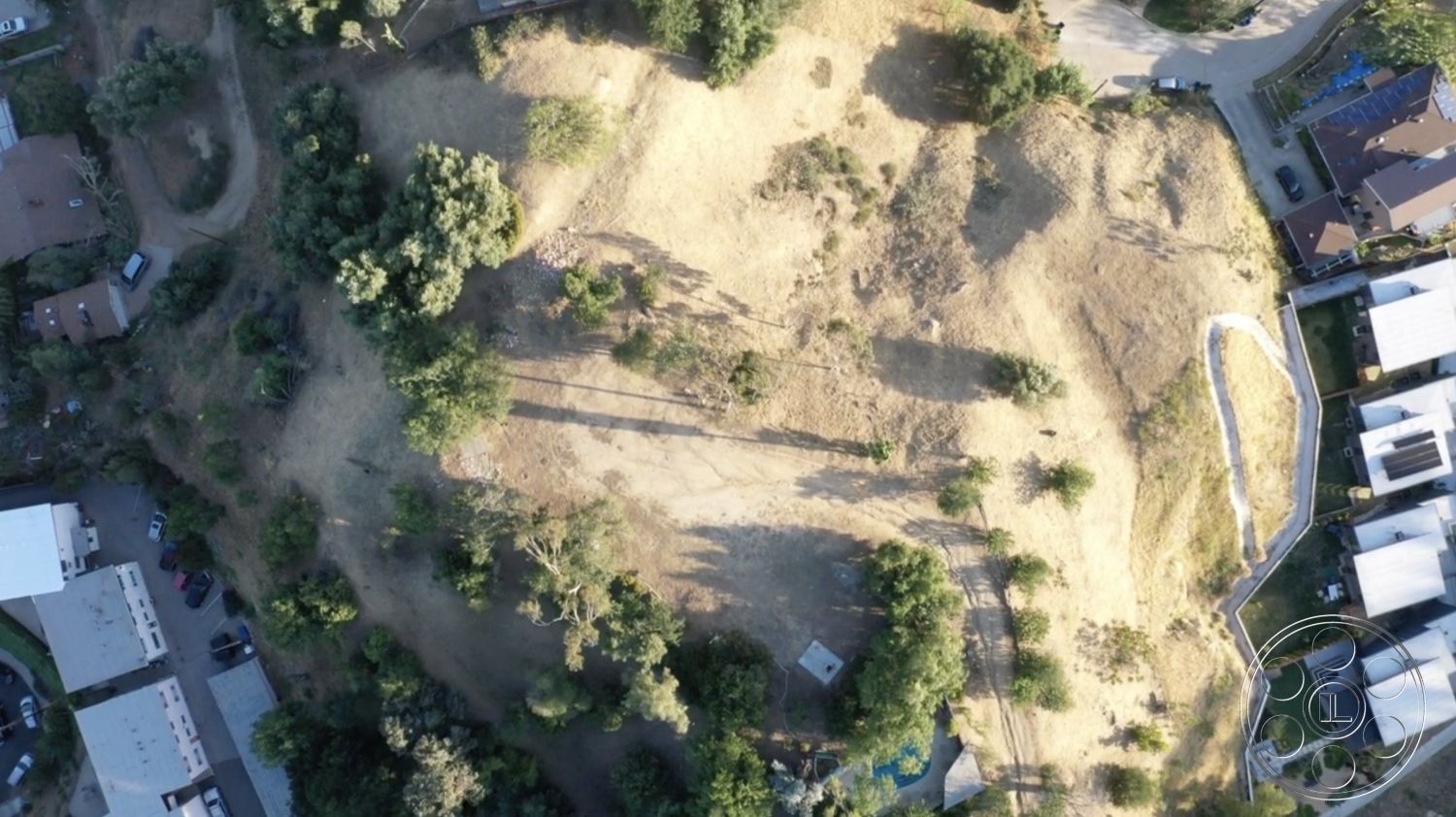 Exotic 36 - earth tones, scattered trees, sloping hillside, natural terrain, undeveloped land, urban-rural transition, surrounding cityscape, sunlit landscape, varied topography, surrounding residential structures, urban neighborhood backdrop, vacant plot with potential, natural grass area, adjacent paved roads, views of nearby homes, potential for landscape design, exterior open space, undeveloped lot ready for construction, mixed-use residential area, optional pool site, future home site location